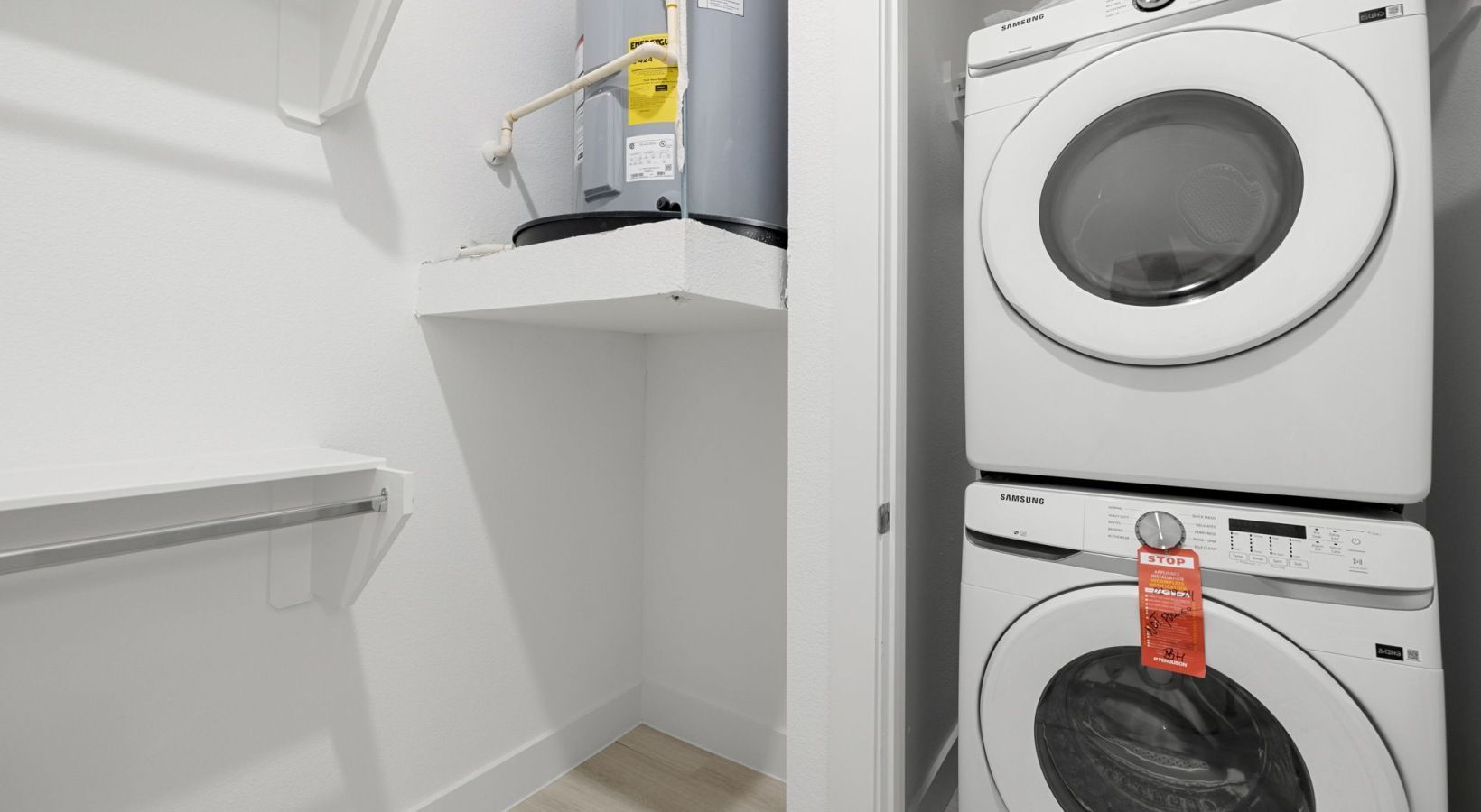 Small laundry closet with stacked white washer and dryer, shelves, and a utility sink.