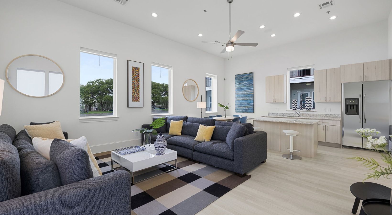 Bright modern living room with gray sofas, patterned rug, and open kitchen with white cabinetry