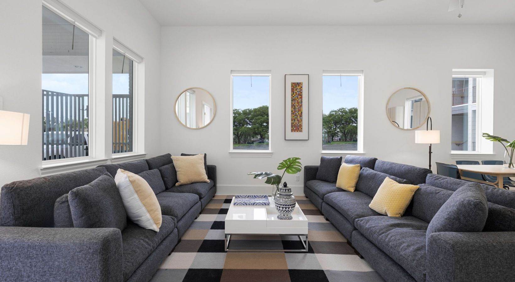 Bright modern living room with two gray sofas, black-and-white rug, coffee table, and wall mirrors