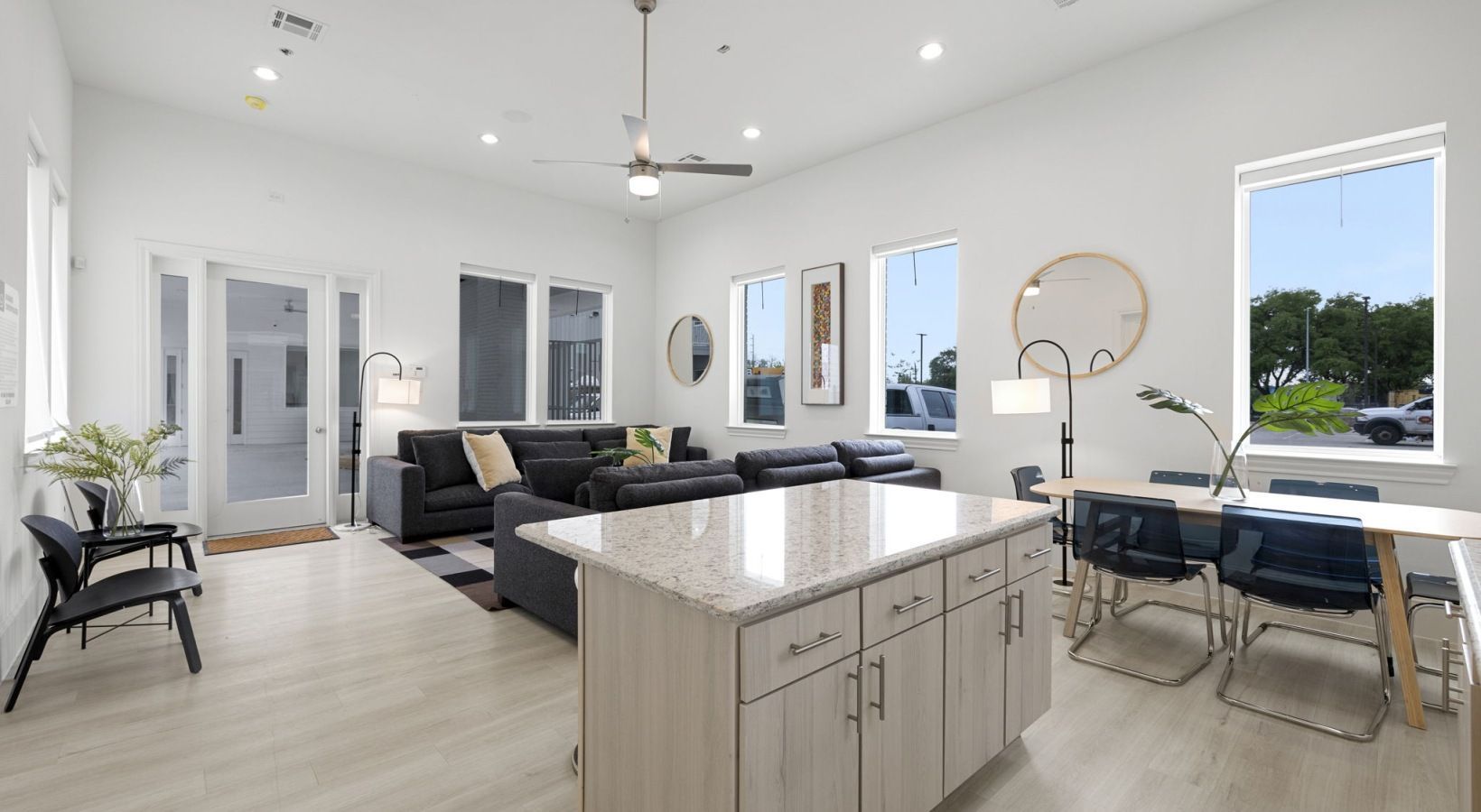 Bright modern open-plan living room with kitchen island, gray sofa, dining table, and large windows