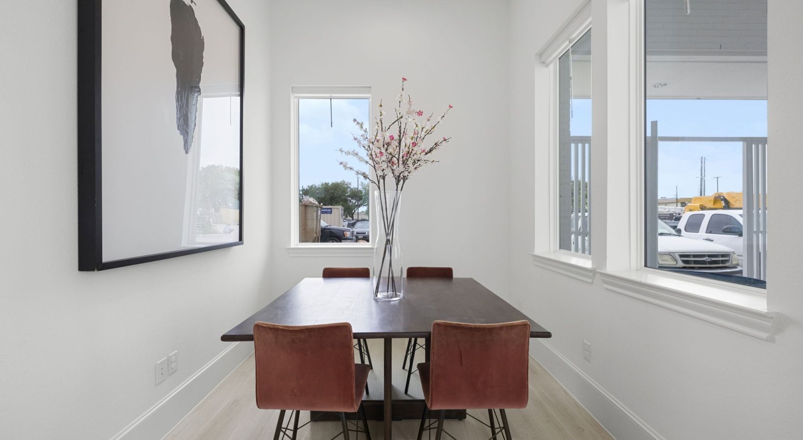 Modern dining nook with dark table, red chairs, vase centerpiece, and bright windows.