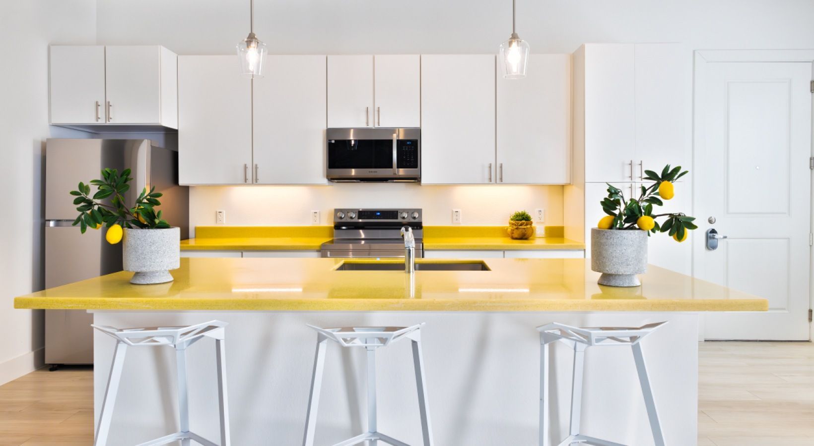 Modern white kitchen with yellow island, stainless steel appliances, and potted plants