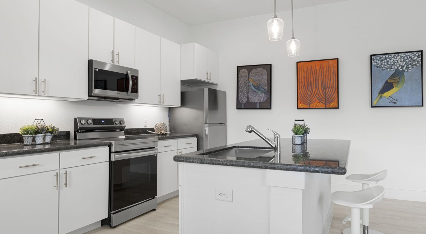 Modern white kitchen with stainless steel appliances, island, hanging lights, and wall art