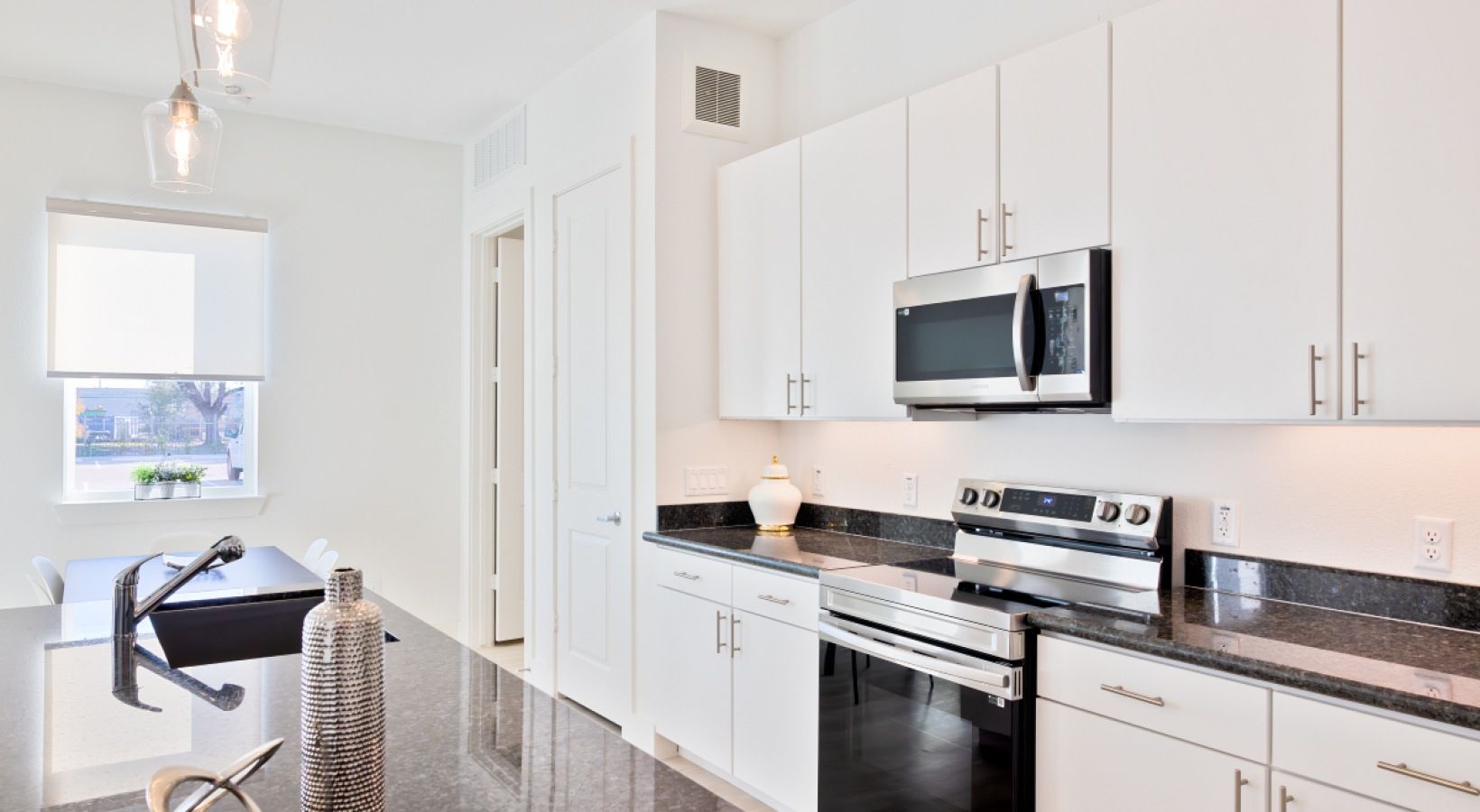 Bright modern white kitchen with stainless steel appliances and black countertops, near a small dining area