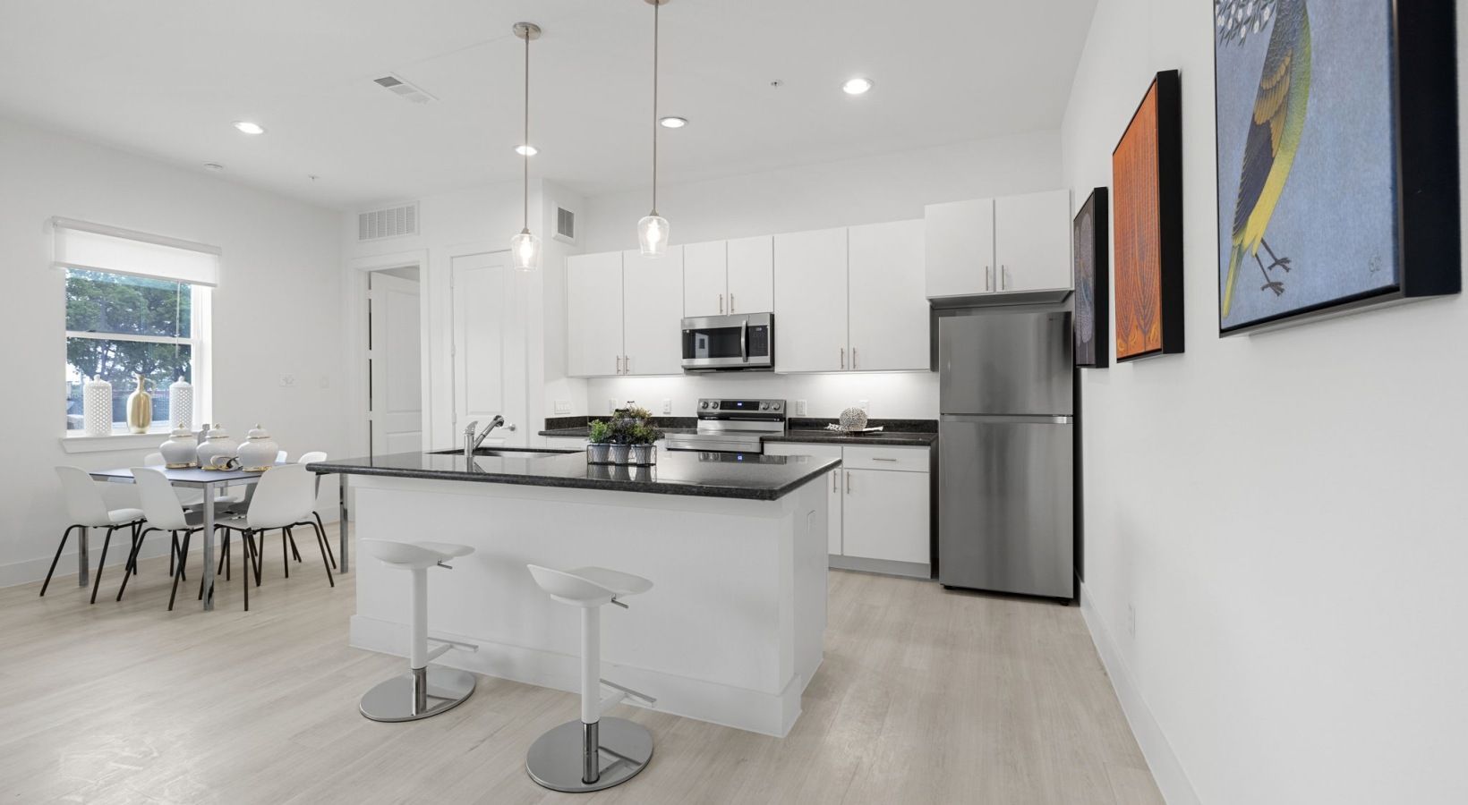 Bright modern kitchen and dining area with white cabinetry, island stools, stainless fridge, and wall art