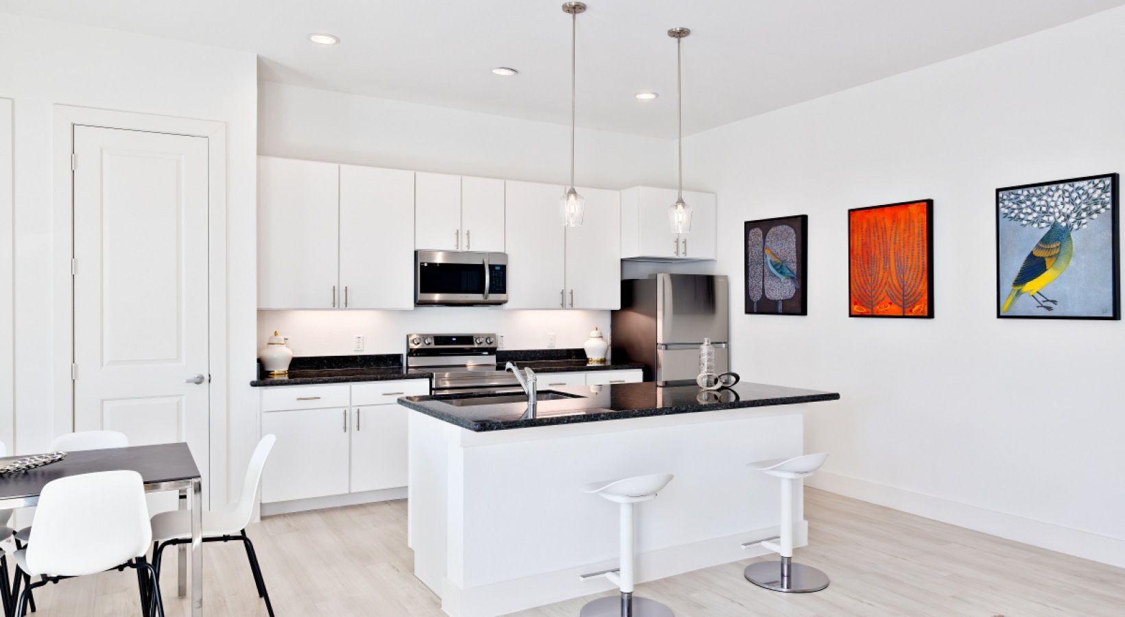 Bright modern kitchen with white cabinets, black countertops, island stools, and colorful wall art