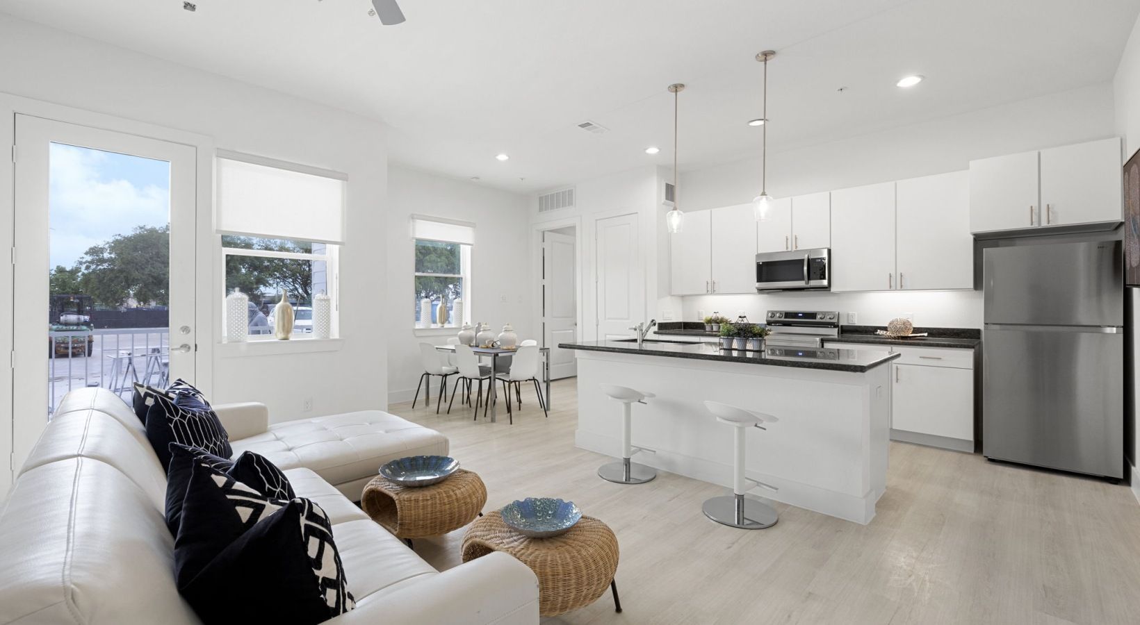 Bright modern kitchen and living area with white cabinets, island, black stools, and sofa by large windows
