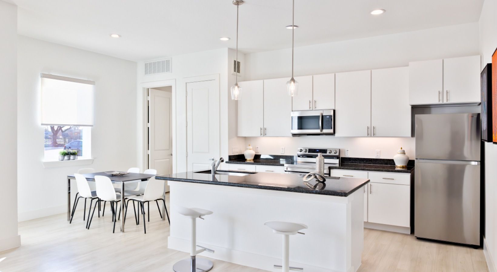Bright modern white kitchen with island, bar stools, dining table, and stainless steel appliances