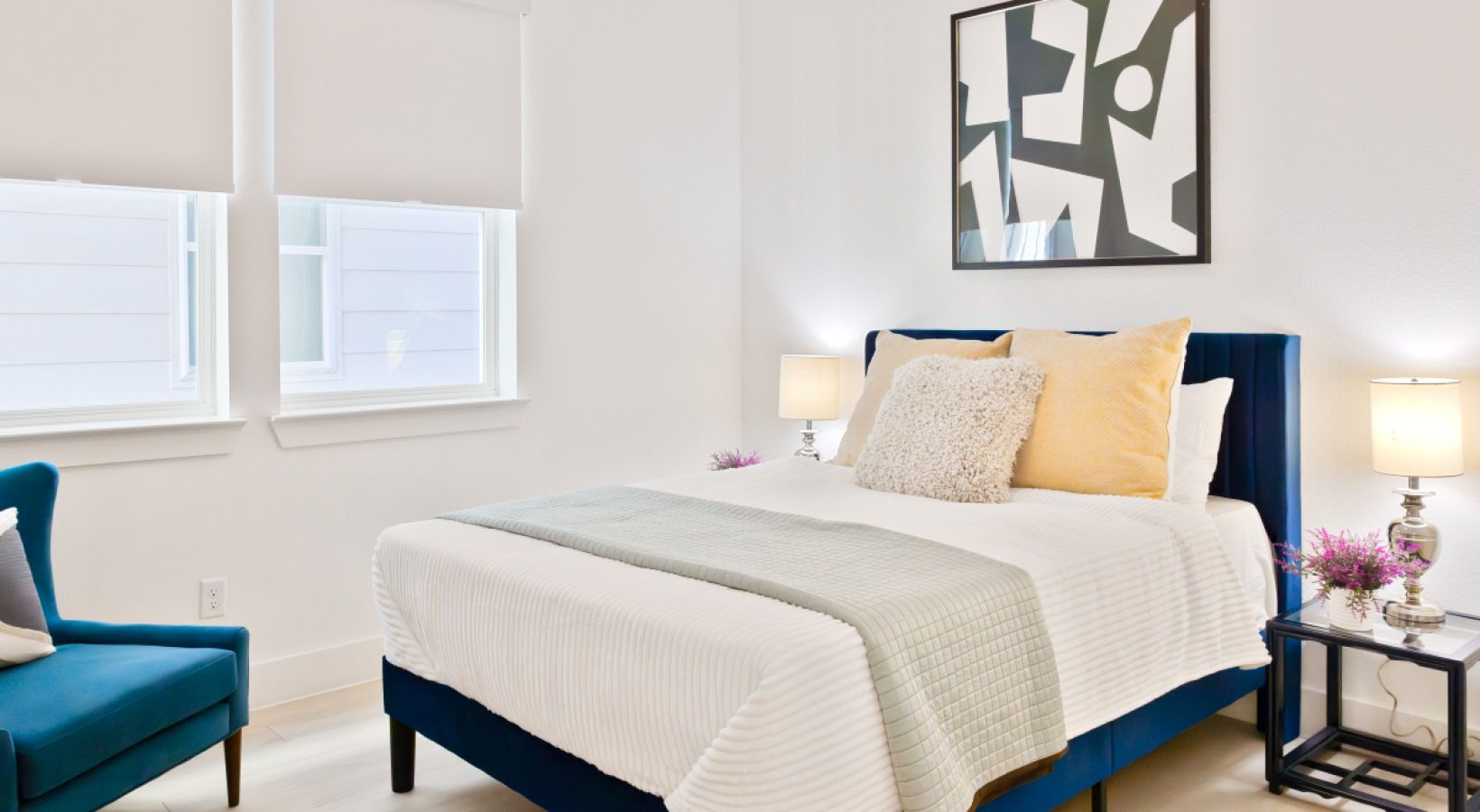 Bright bedroom with white bed, navy headboard, teal chair, and abstract wall art