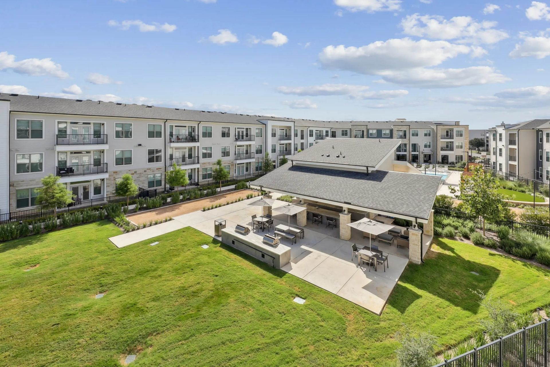 Modern apartment complex with a grassy courtyard and covered outdoor pavilion under a blue sky