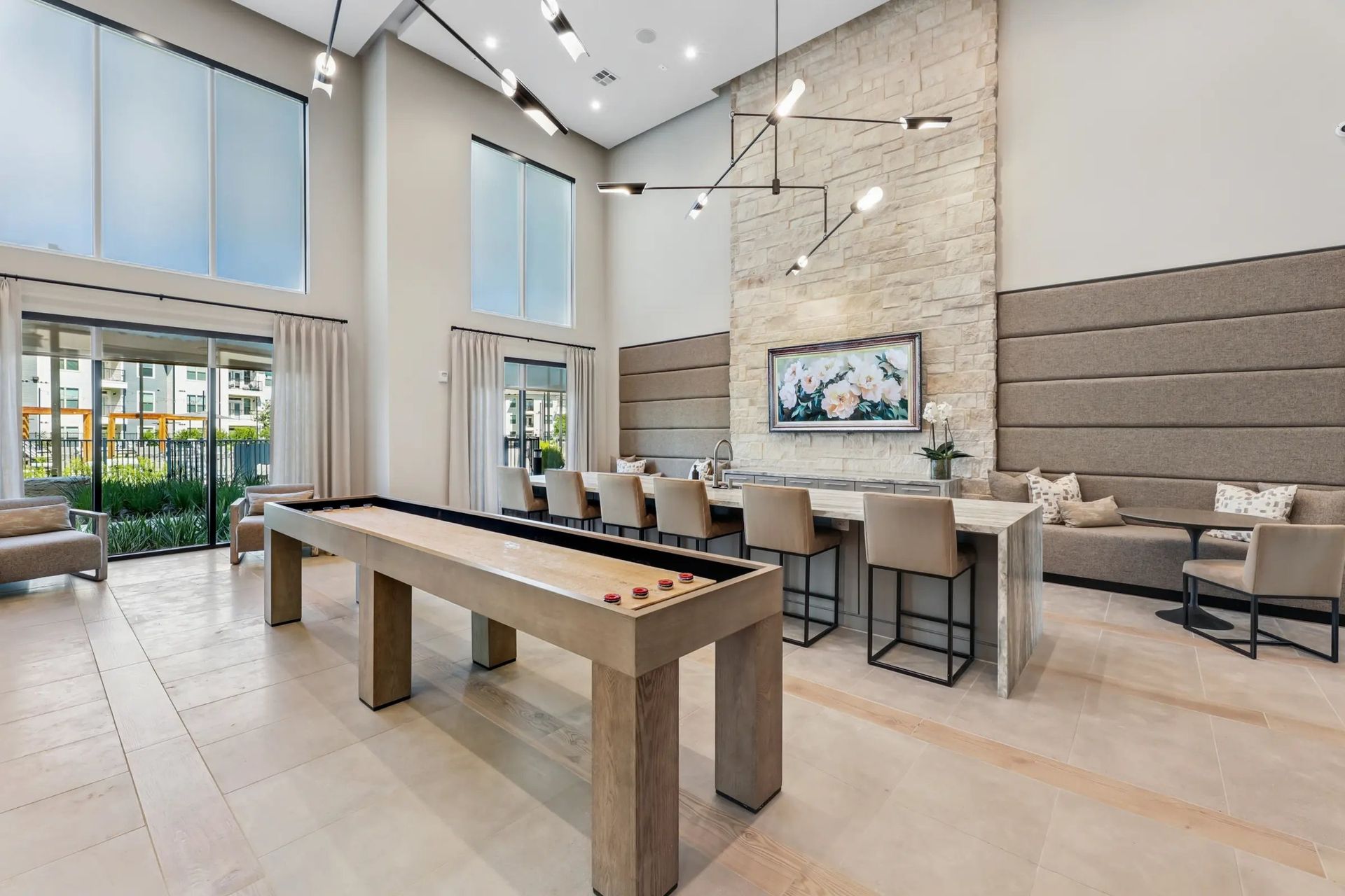 Bright modern lounge with high ceilings, large windows, stone walls, and a long dining table