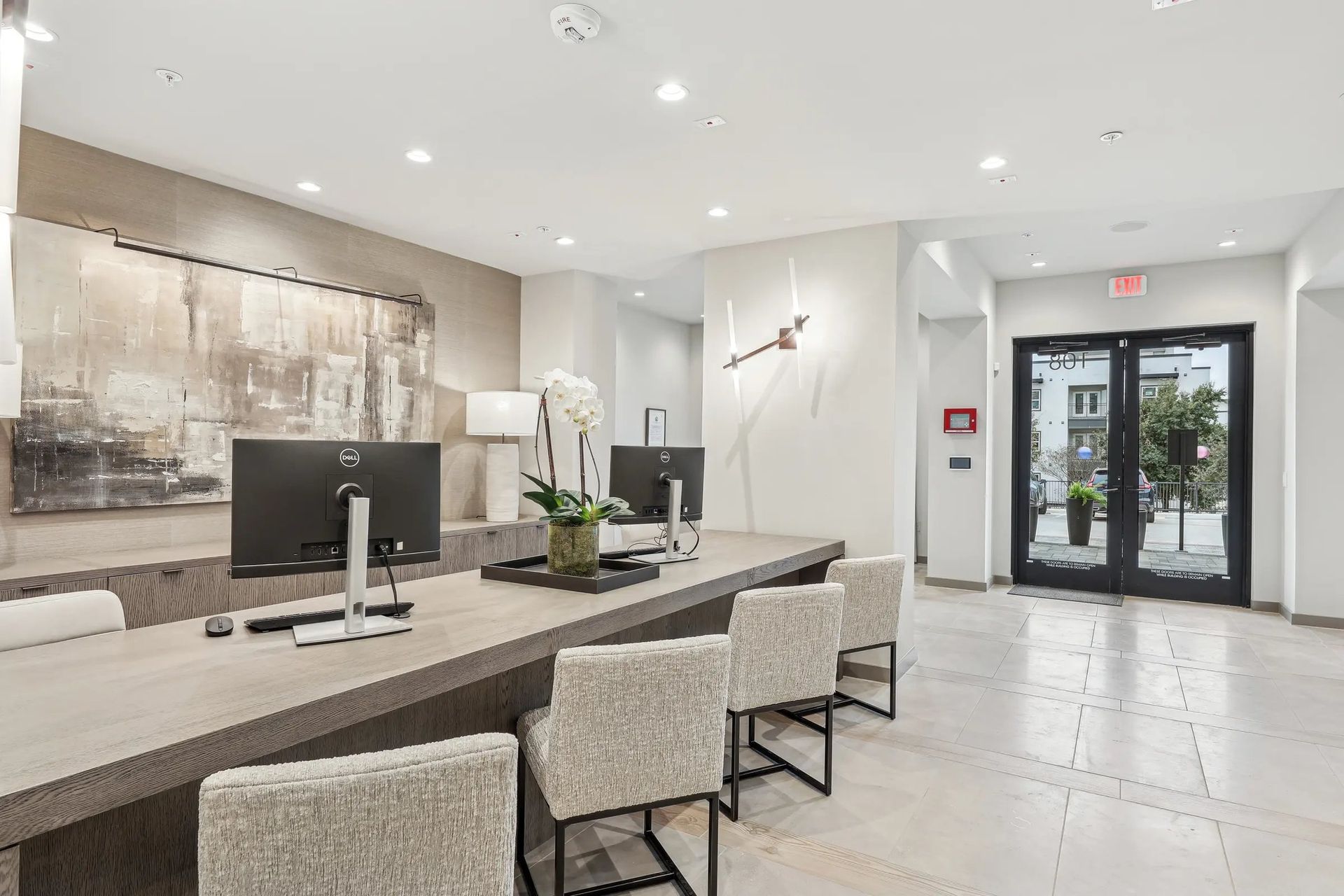 Modern apartment lobby with a reception desk, seating, wall art, and glass entrance doors