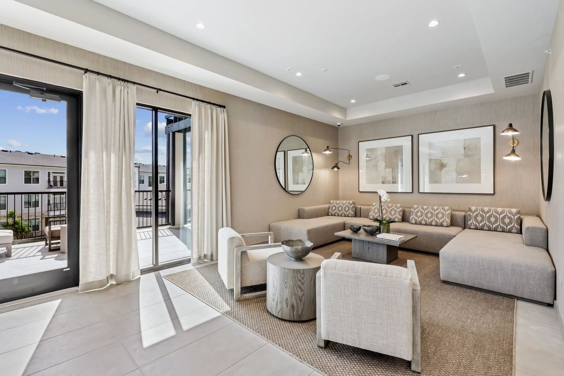 Bright modern living room with sectional sofa, round table, wall art, and open sliding doors to a patio.