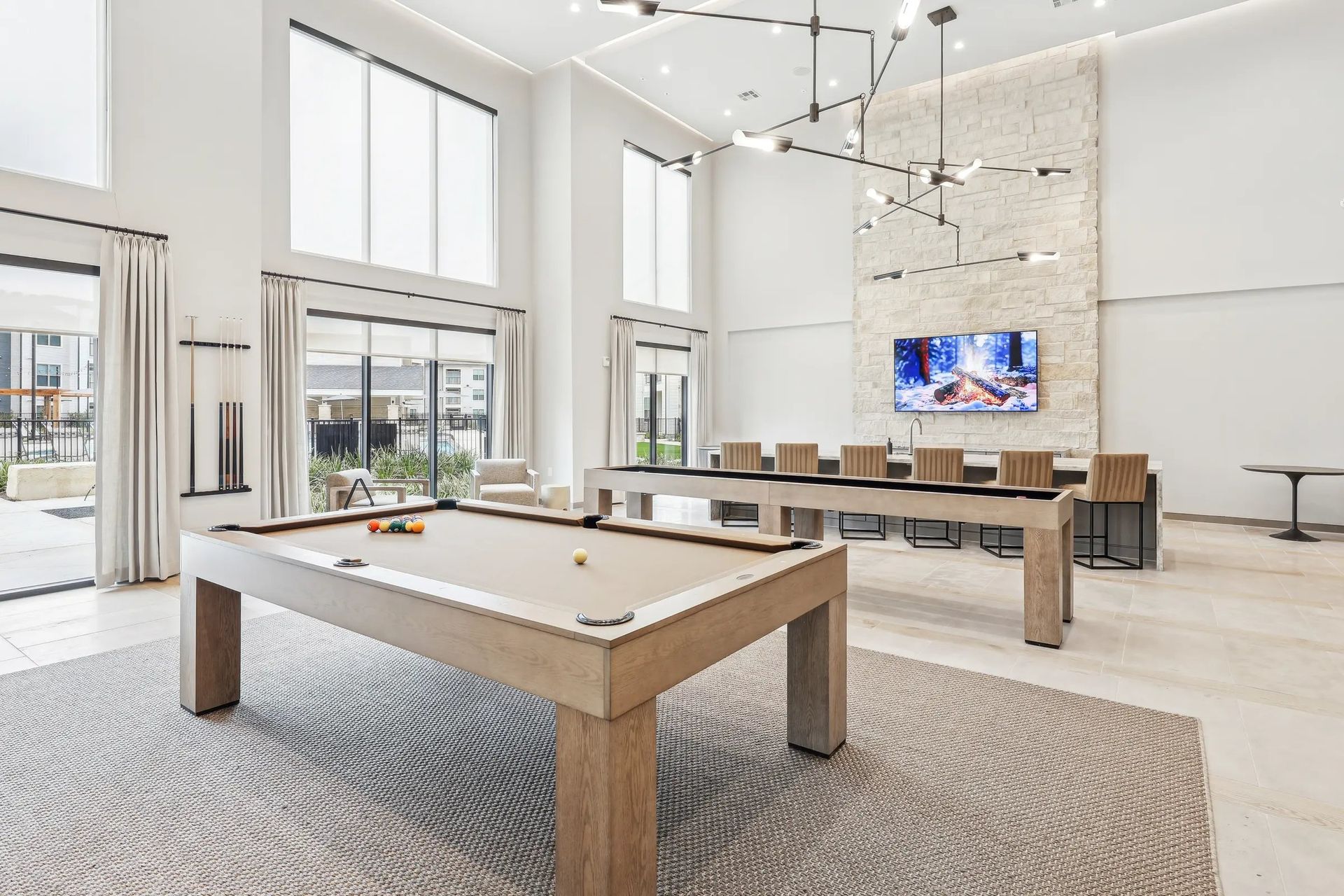 Bright modern living room with large windows, a stone fireplace, and a pool table in the foreground