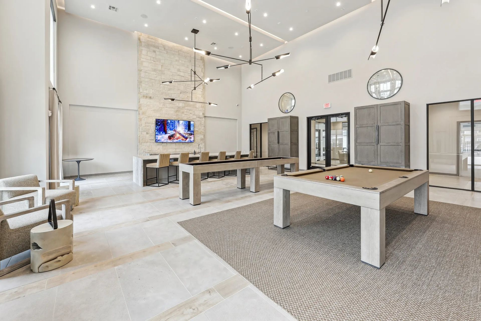 Spacious modern living room with high ceilings, gray seating, wood tables, and a TV on the wall.