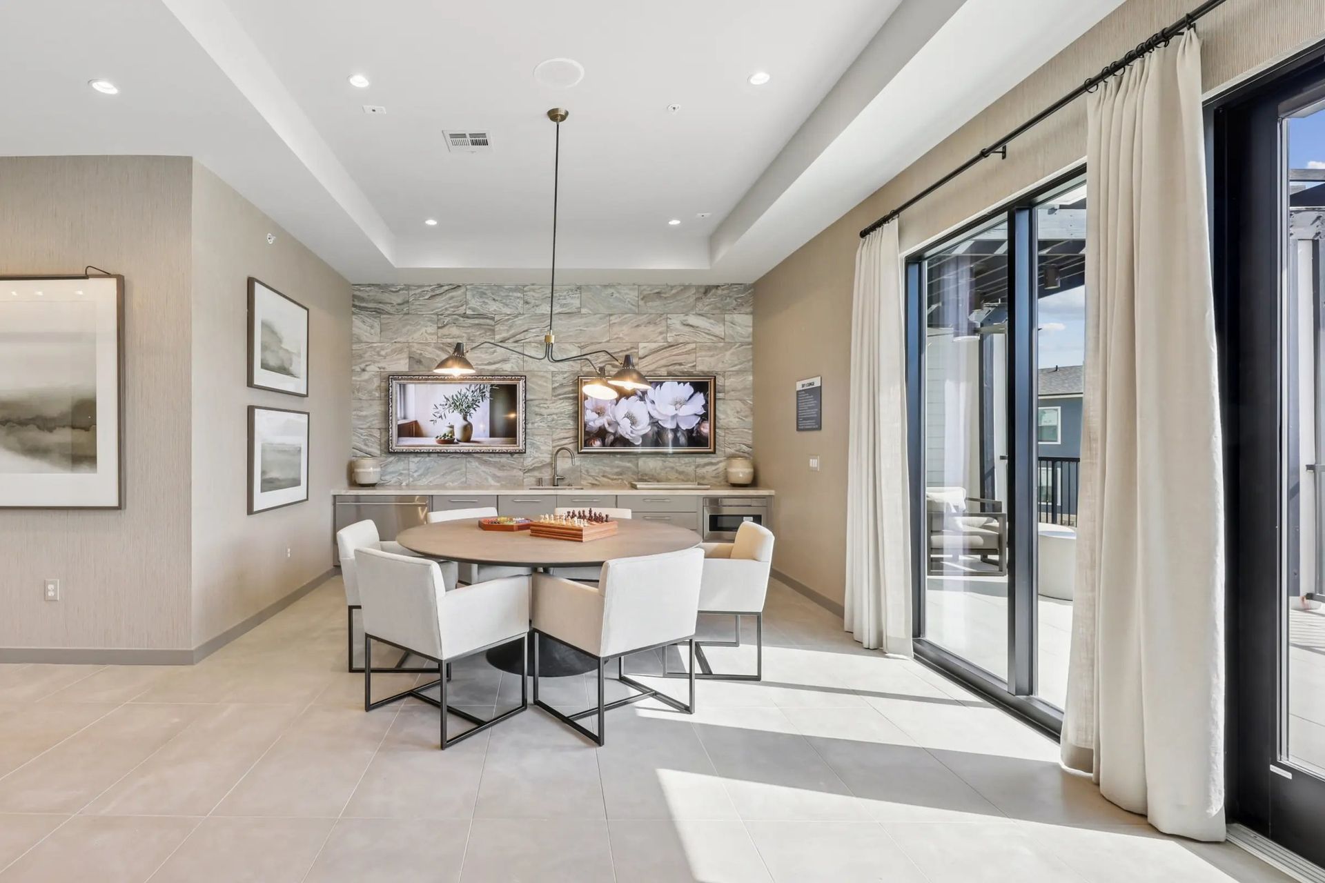 Bright modern dining area with white chairs, stone accent wall, and large sliding glass doors.
