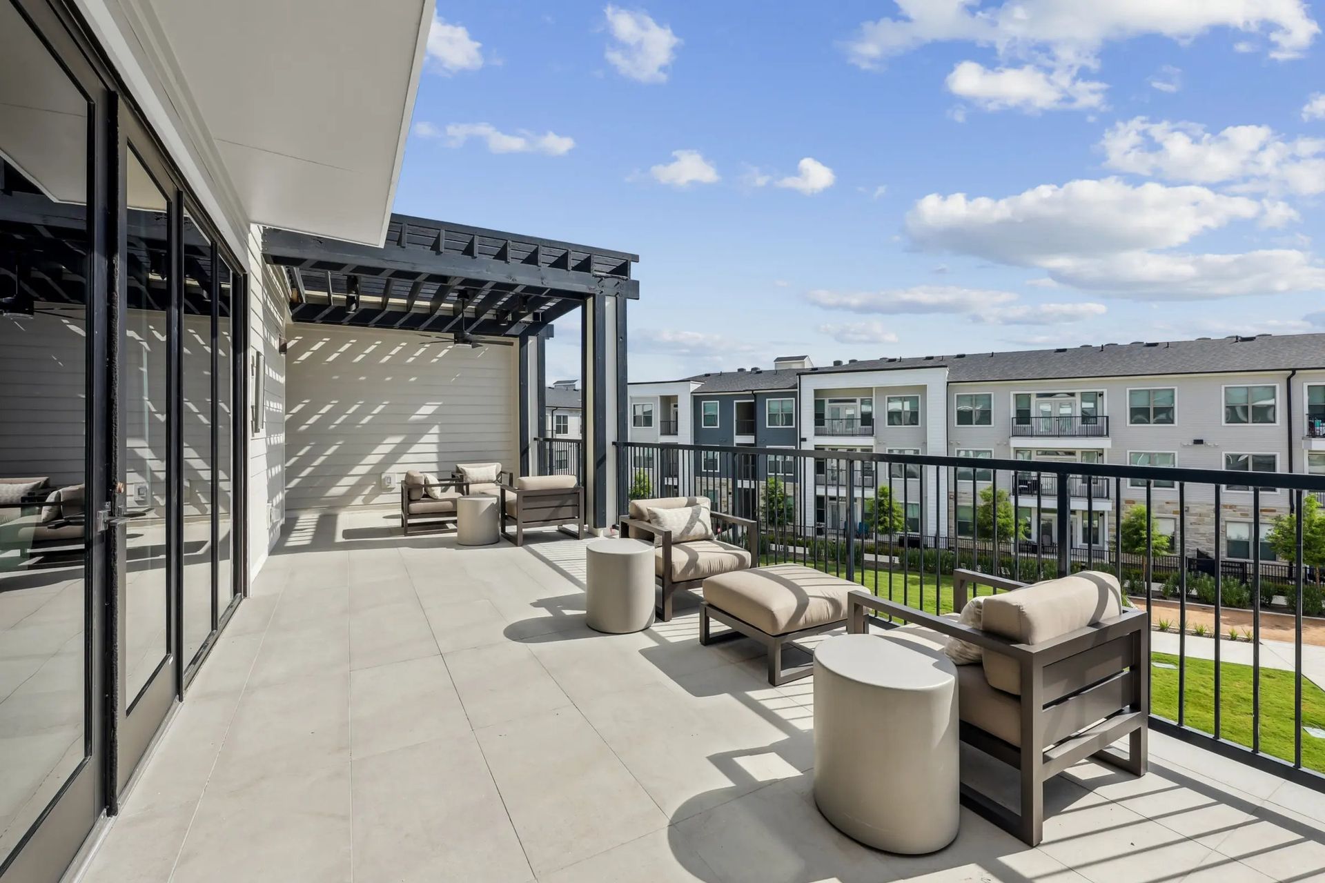 Modern apartment balcony with lounge seating, pergola, and view of neighboring buildings