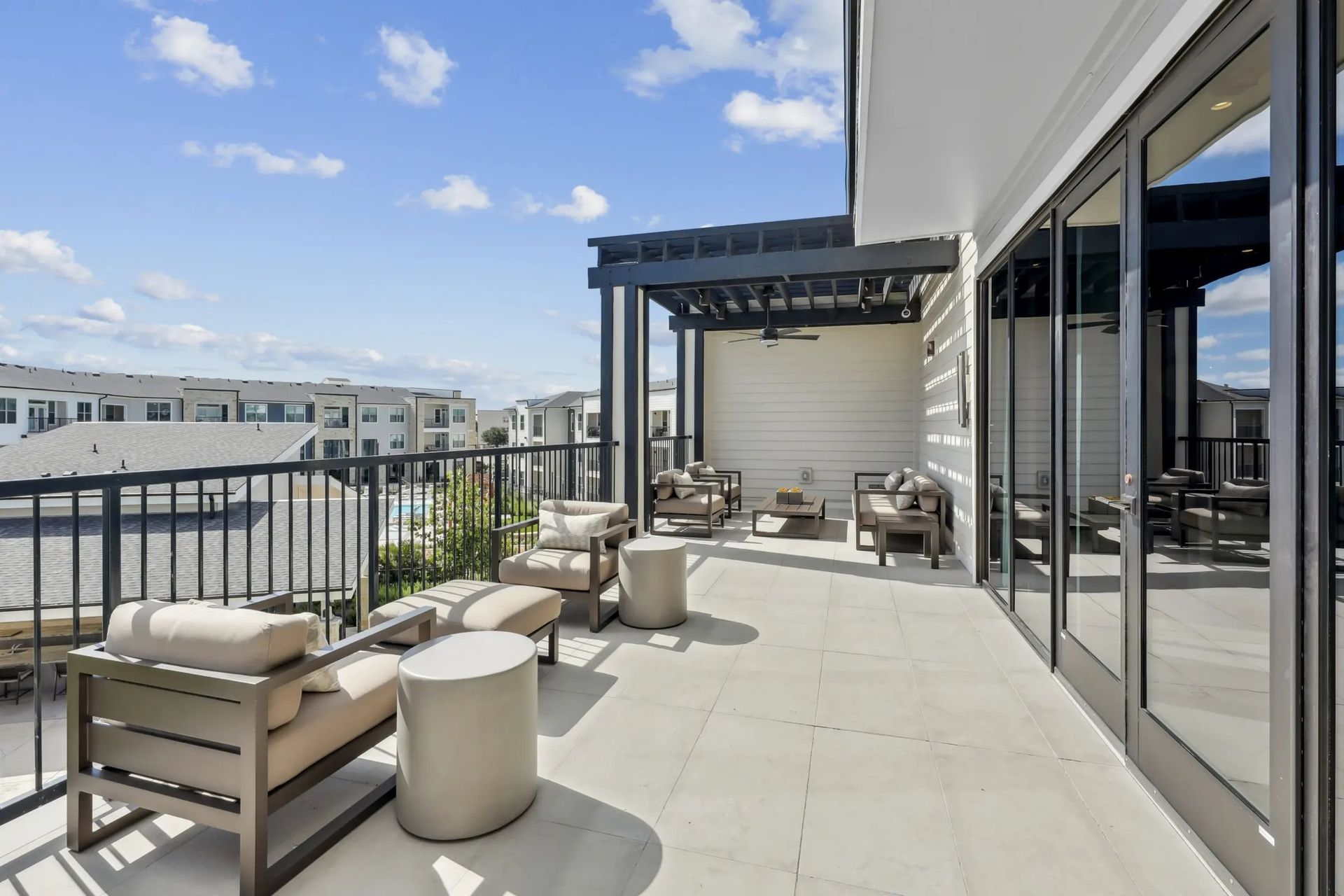 Rooftop patio with beige lounge chairs, tables, and city view under a blue sky
