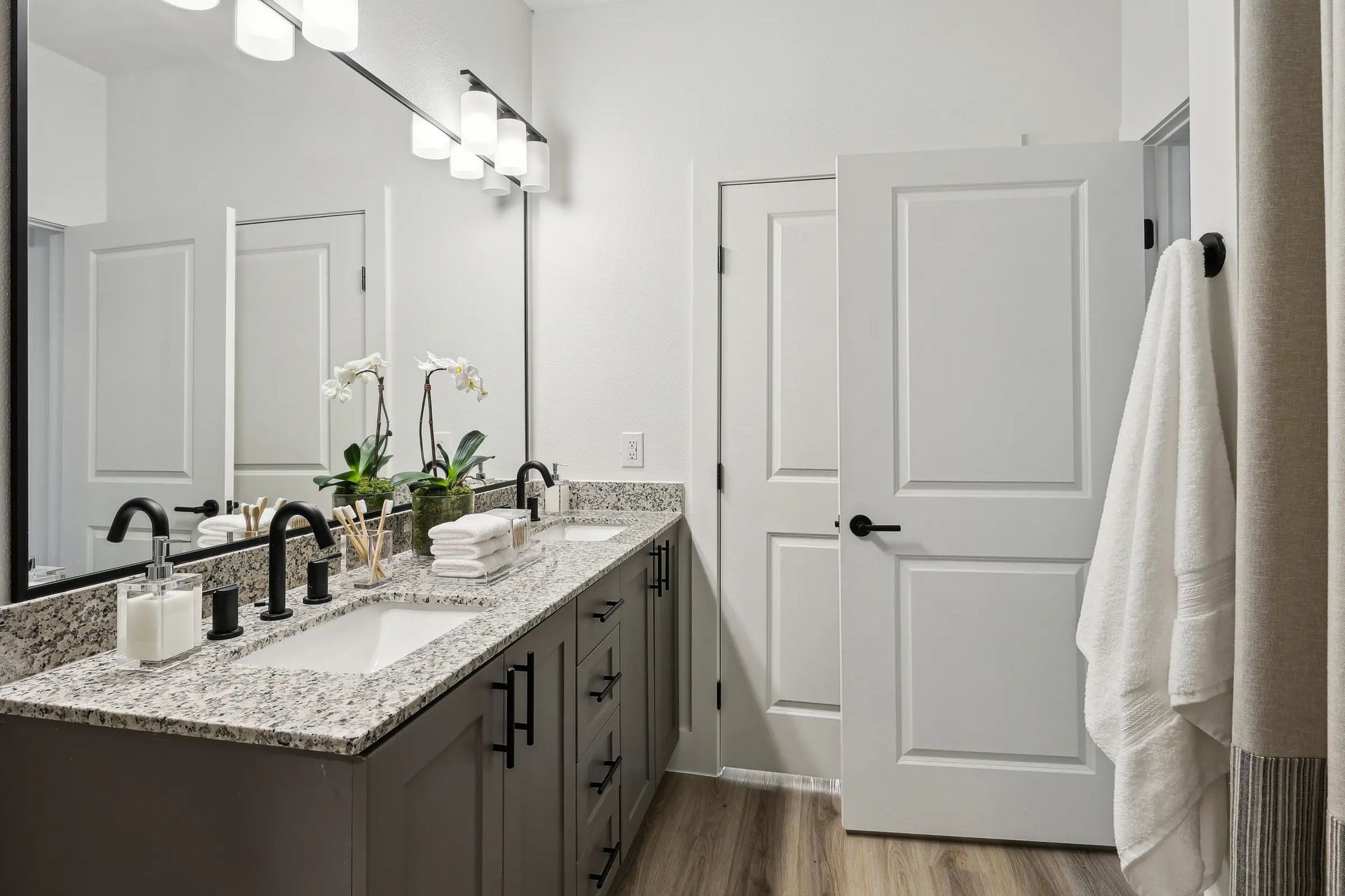 Bright modern bathroom with double vanity, large mirror, and white door and towels