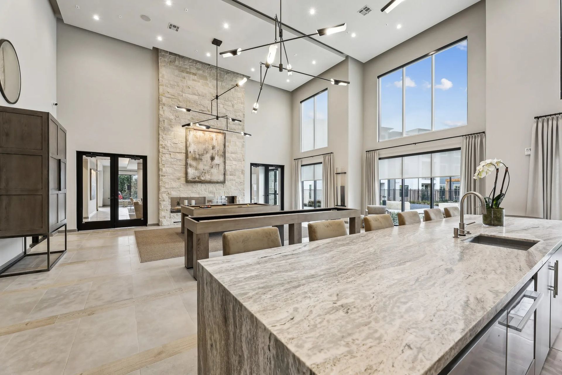 Bright modern living room with vaulted ceiling, large windows, and beige stone island in foreground
