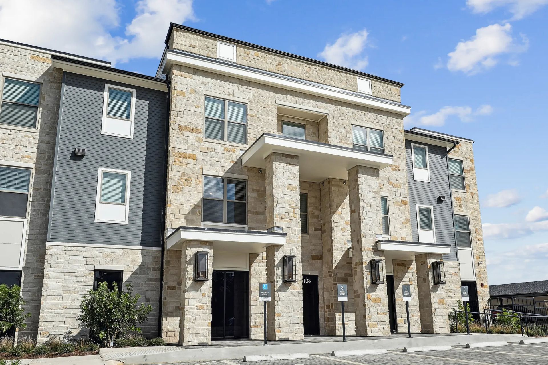 Modern apartment building exterior with stone and gray facade under a blue sky