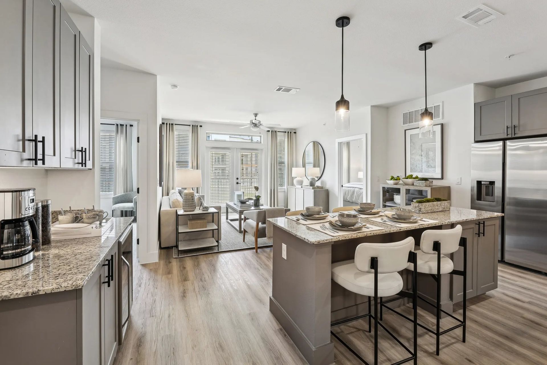 Bright modern kitchen with granite island, white cabinets, bar stools, and open living area