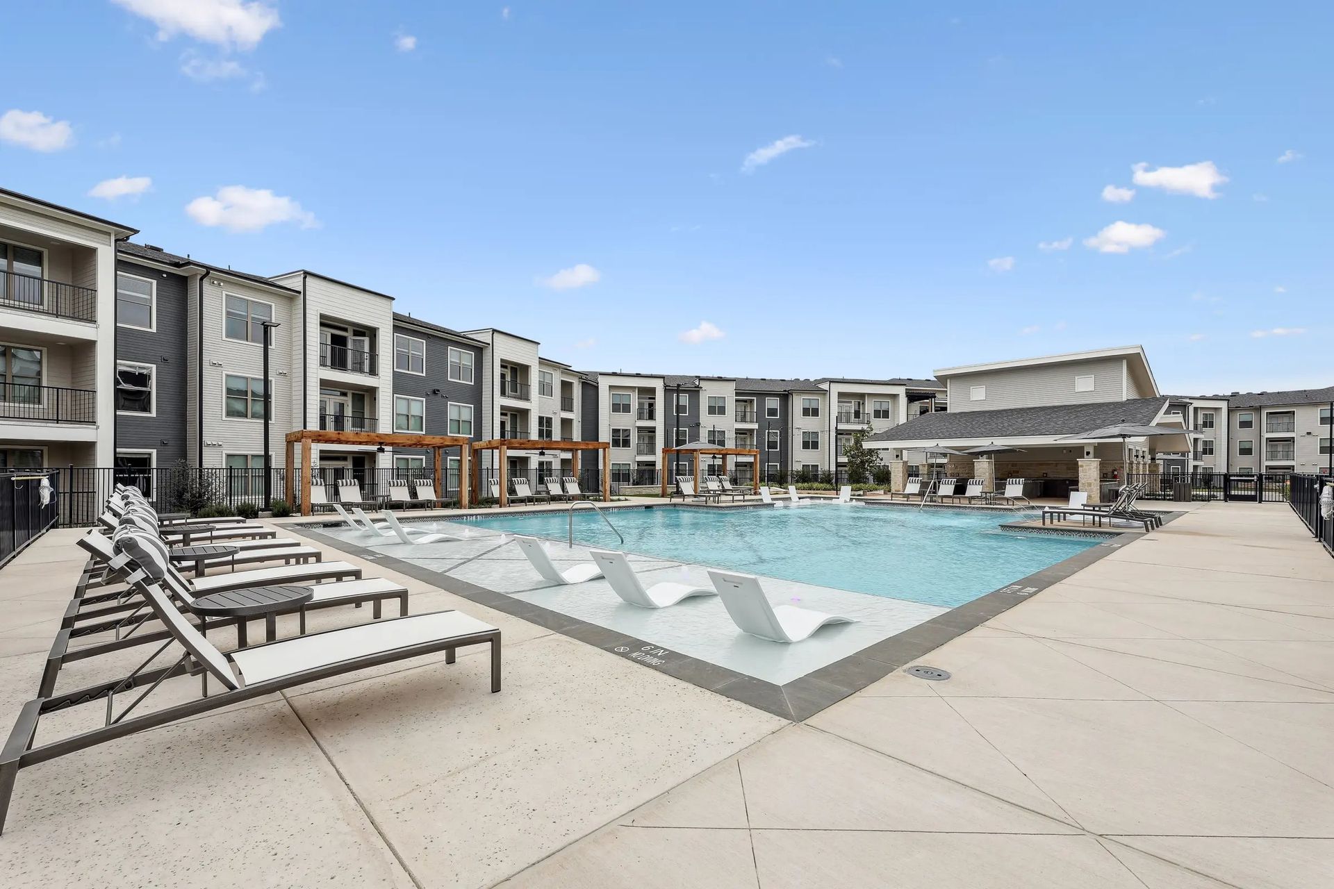Modern apartment courtyard with a swimming pool and lounge chairs under a blue sky