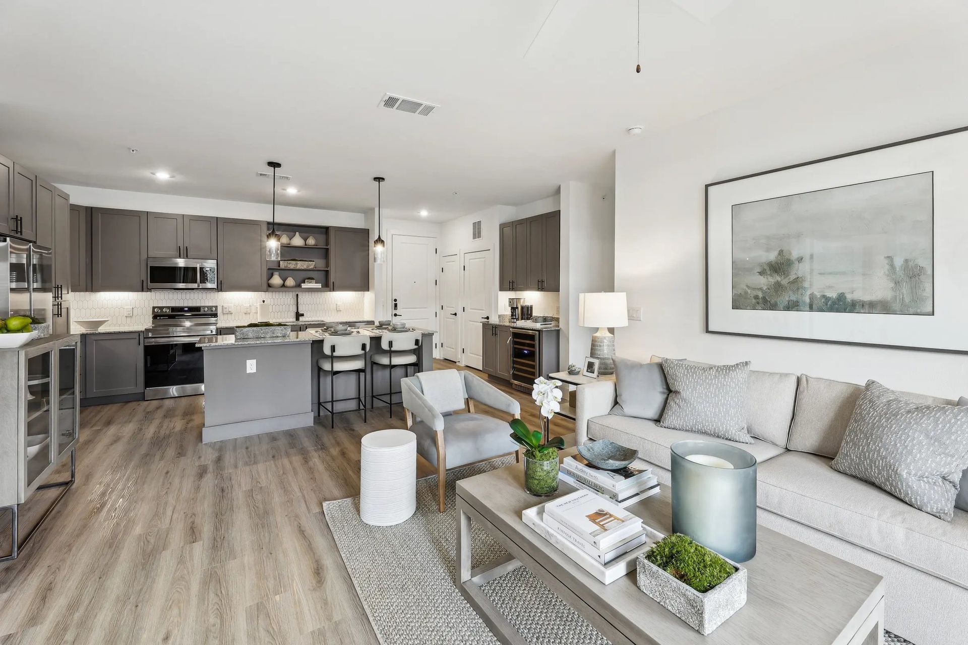 Open-concept living room and kitchen with gray sofa, coffee table, and white cabinetry.
