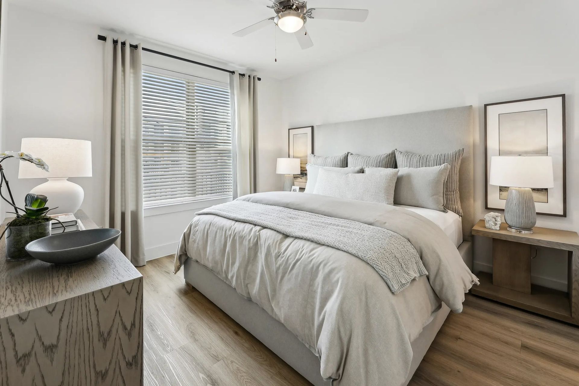 Bright bedroom with a gray bed, nightstands, lamps, and a window with blinds