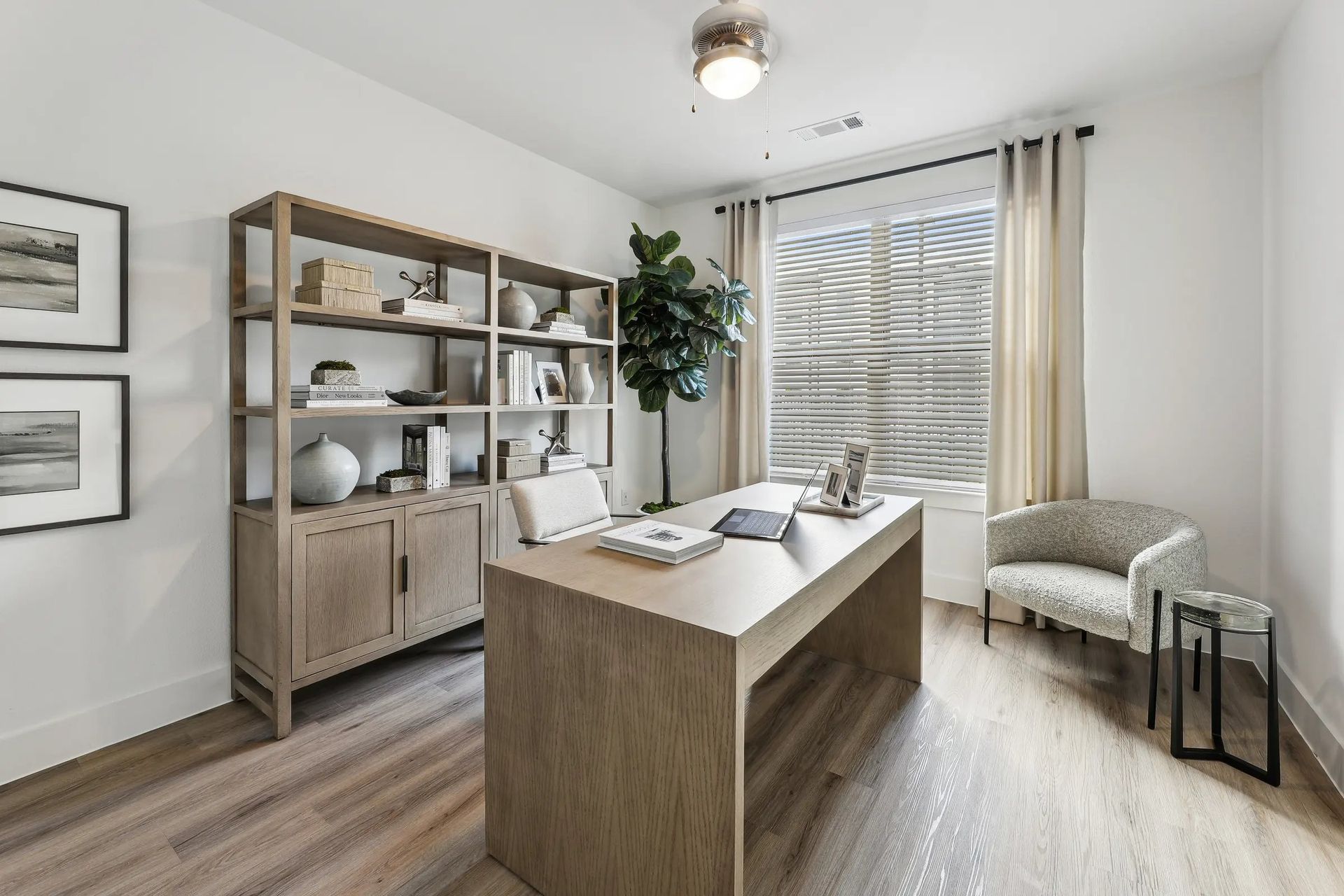 Bright home office with wooden desk, shelving, laptop, and a window with curtains