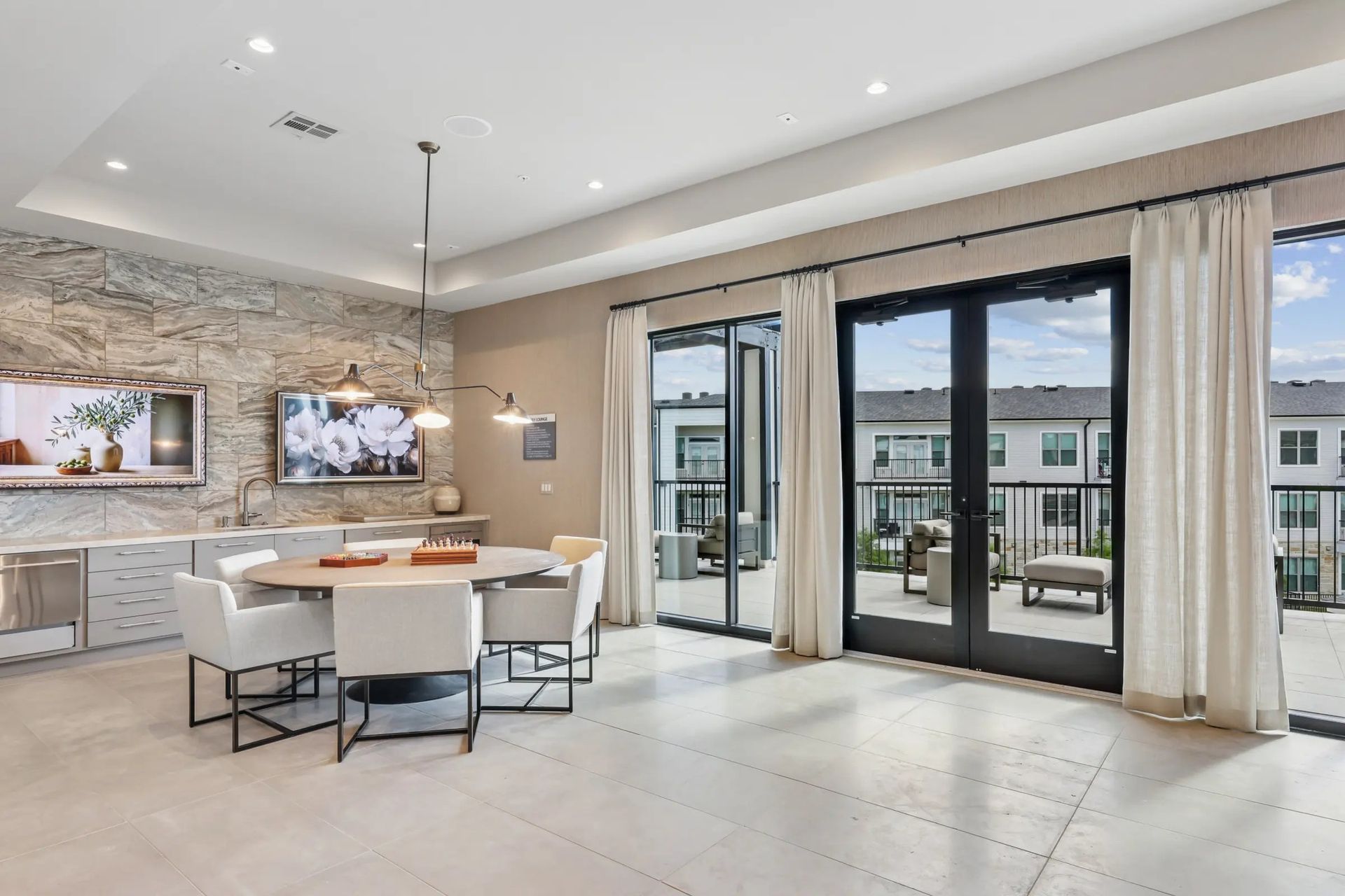 Modern open-plan living area with dining table, sectional sofa, wall art, and large sliding glass doors to a balcony
