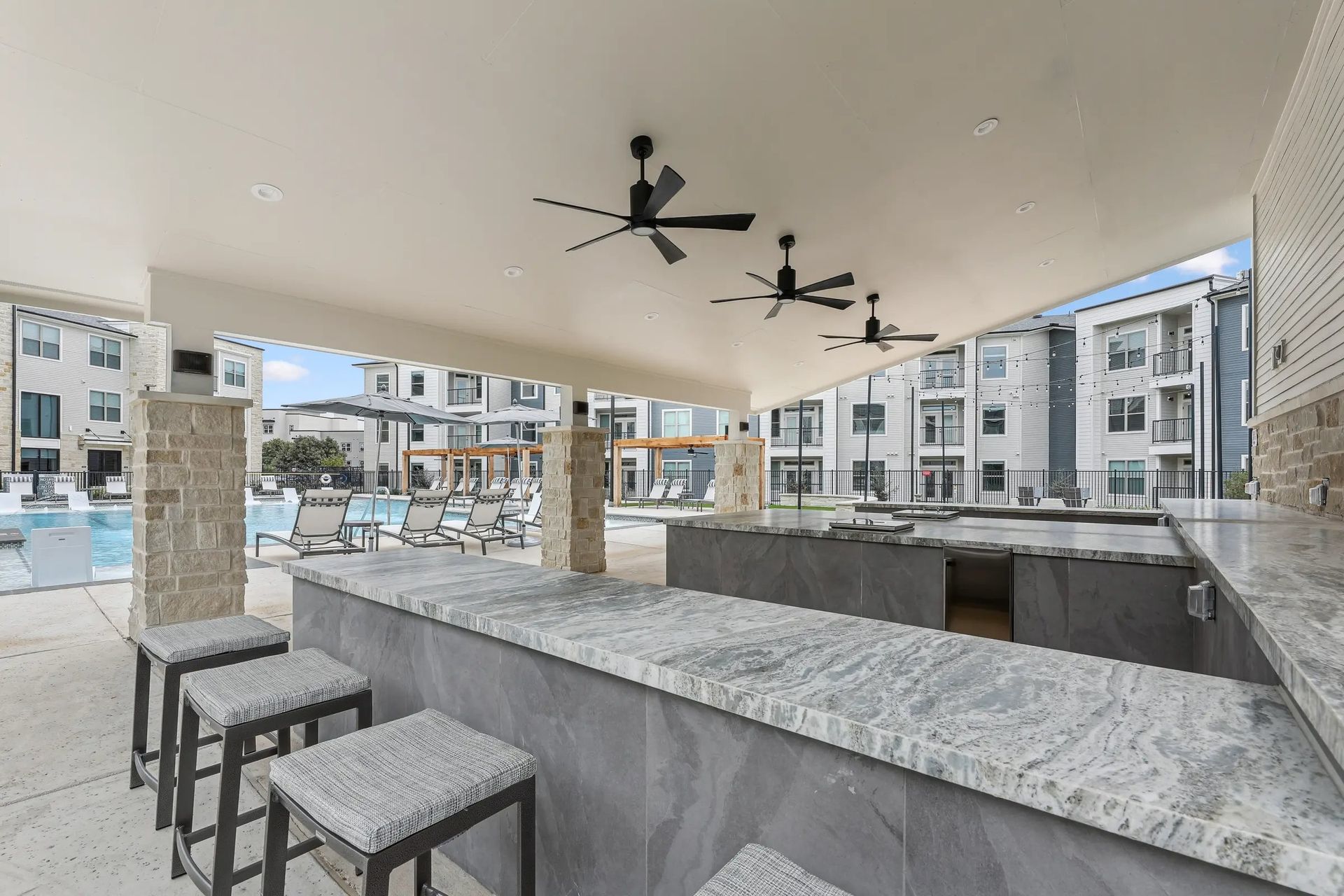 Outdoor apartment courtyard bar with granite counter, stools, and ceiling fans under a covered patio