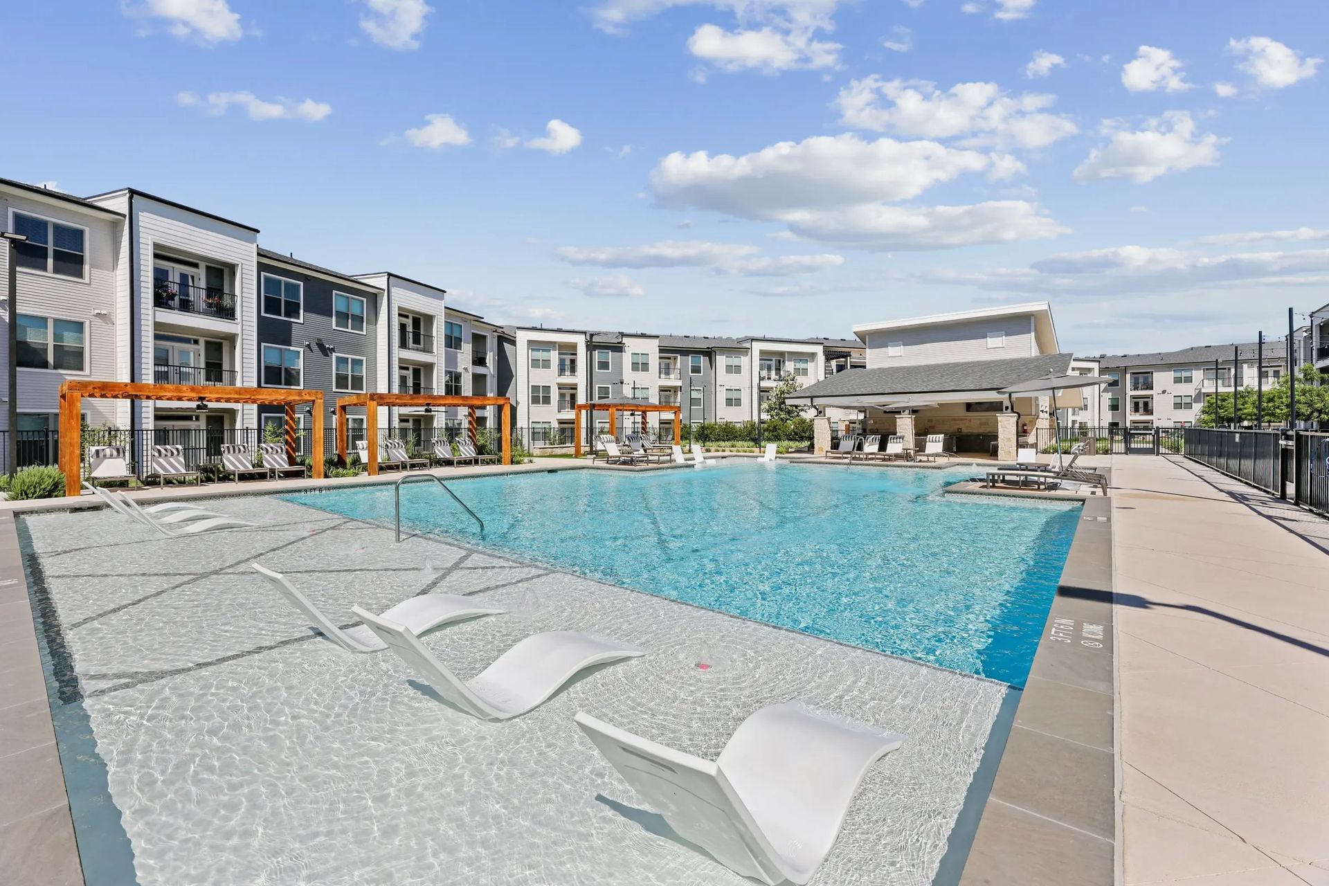 Modern apartment courtyard with a blue pool, lounge chairs, and orange play structure under a bright sky
