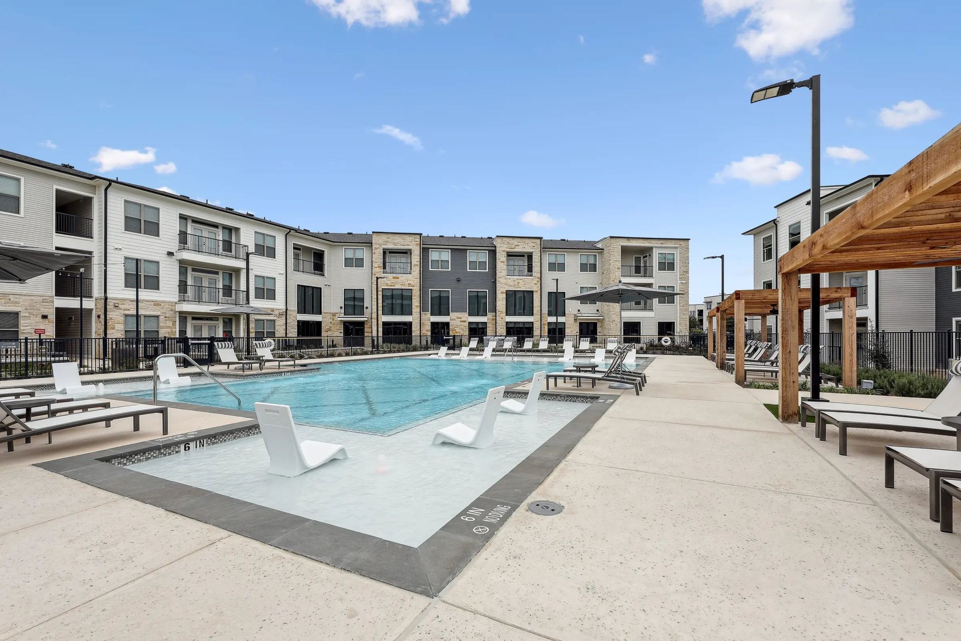 Modern apartment pool courtyard with lounge chairs, umbrellas, and a pergola under a blue sky