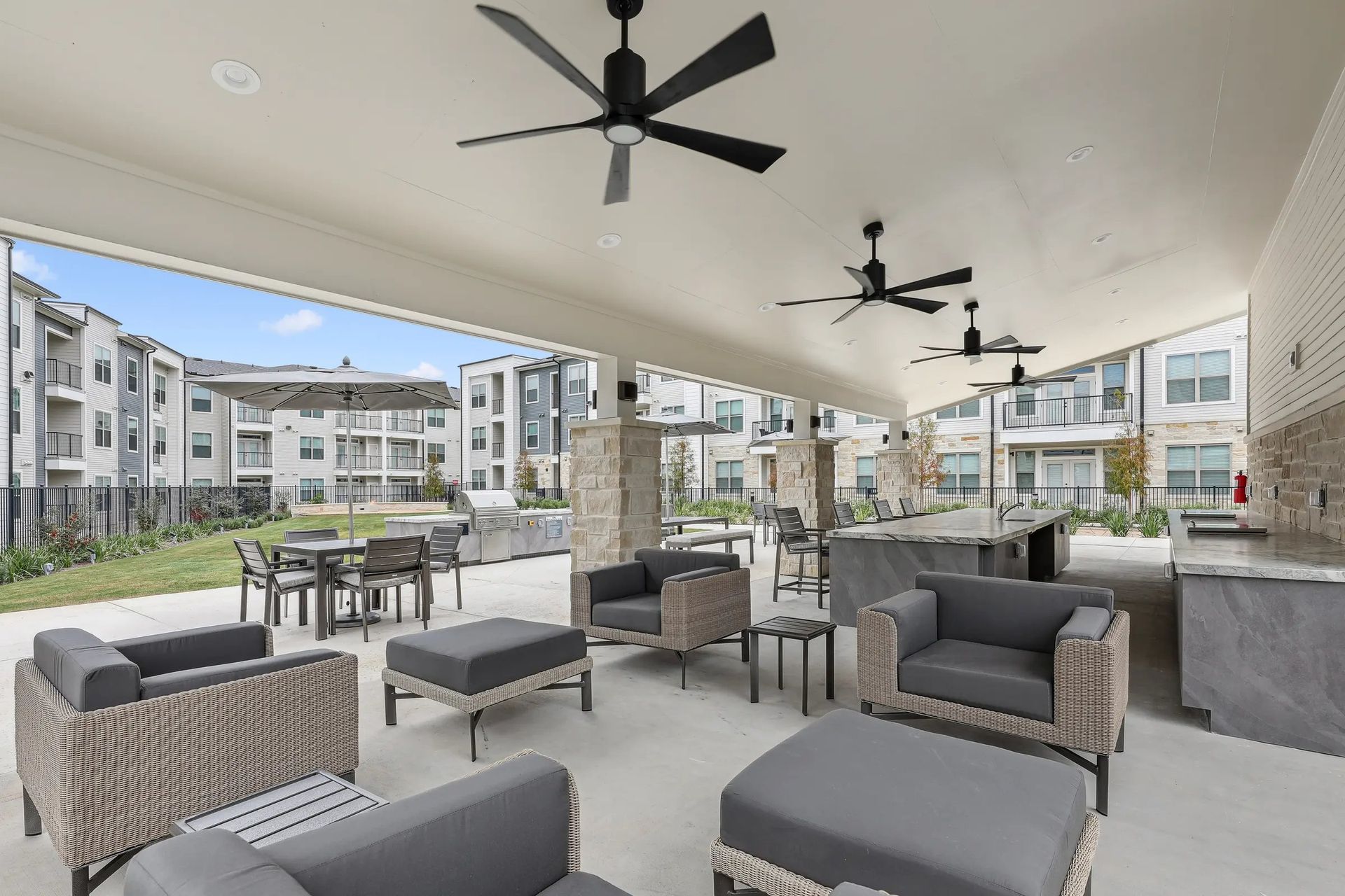 Covered outdoor lounge with gray seating, ceiling fans, and apartment buildings in the background