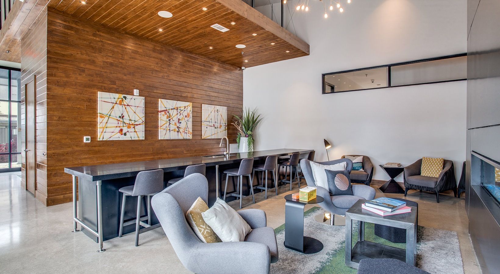 Modern open-plan living room with brick accent wall, gray seating, and a dining area with bar stools