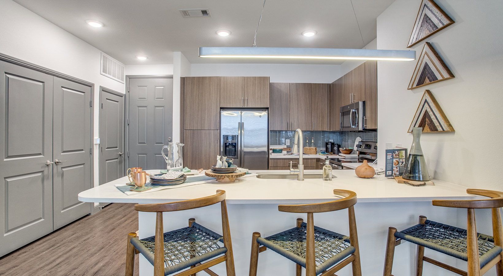 Modern kitchen with white island, wood cabinets, bar stools, and decorative wall art under bright lighting