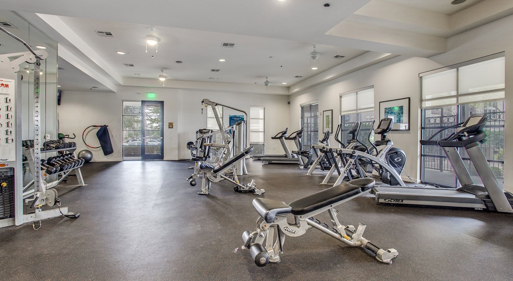Bright gym with treadmills, weight machines, and benches on a black rubber floor