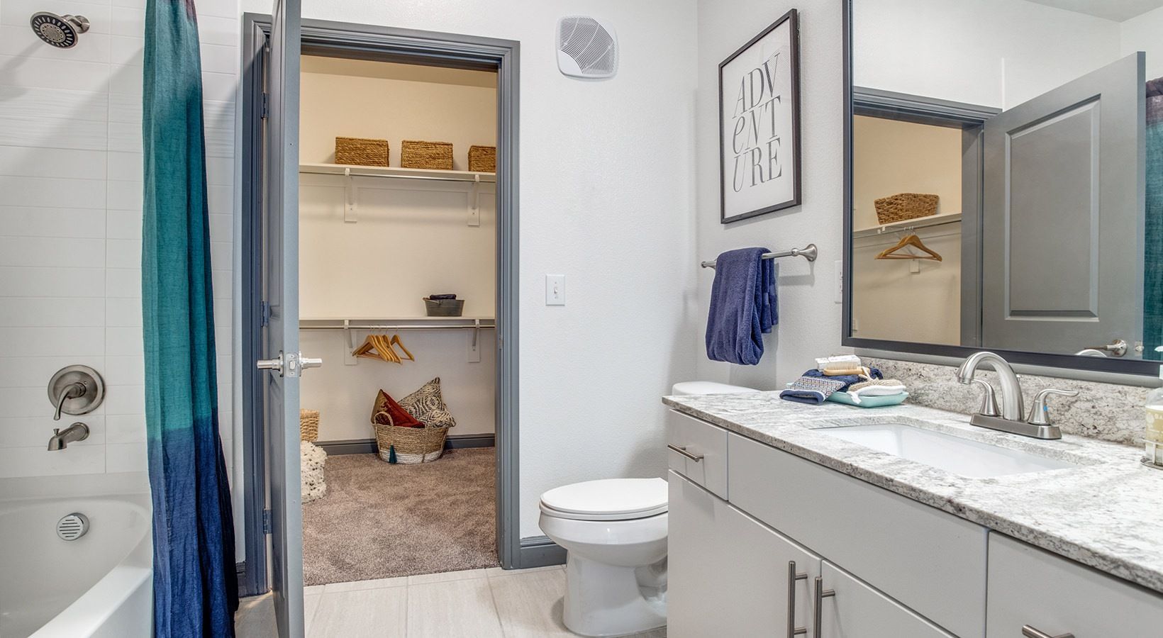 Bathroom vanity beside open doorway to a closet with shelves and hanging clothes
