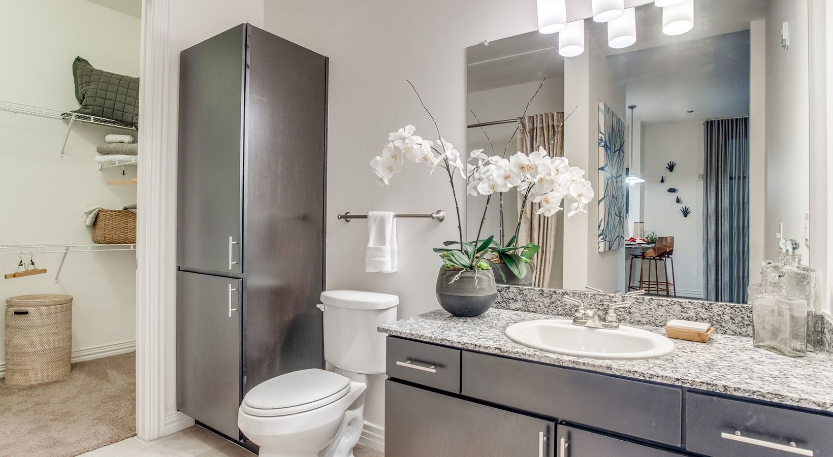 Modern bathroom with dark vanity, large mirror, white orchid, toilet, and glass shower door