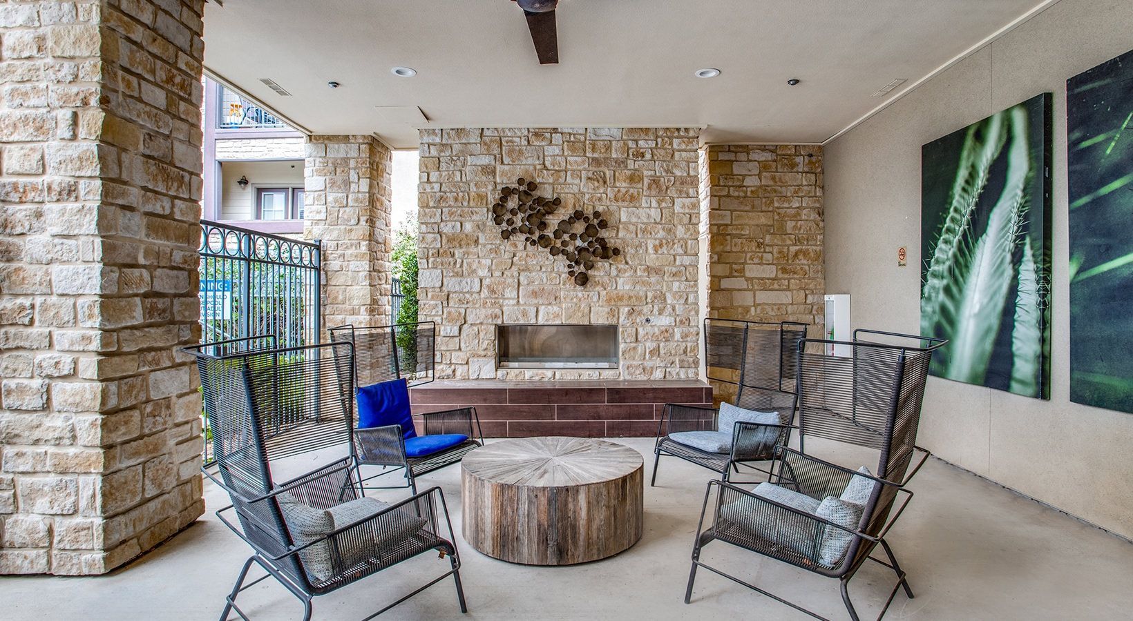 Covered outdoor seating area with stone fireplace, metal chairs, and a round wooden table