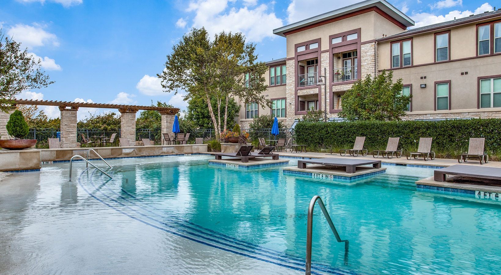Outdoor hotel pool with clear blue water, lounge chairs, and a multi-story building in the background