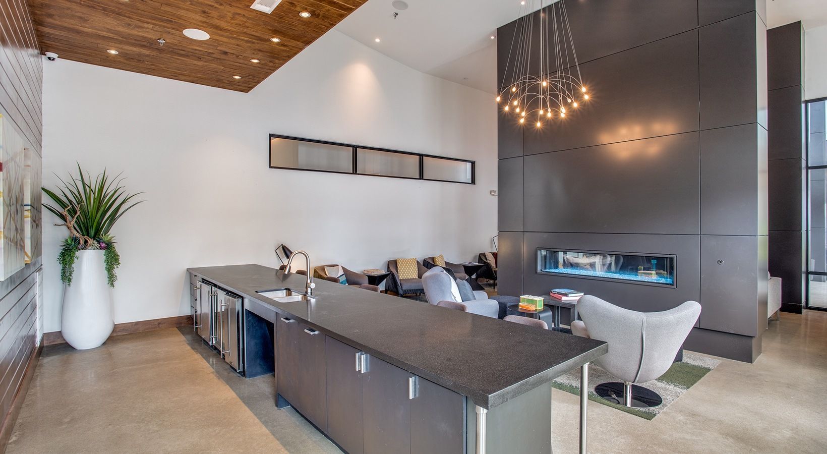 Modern office lounge with a long conference table, white chairs, dark wall, and wood ceiling