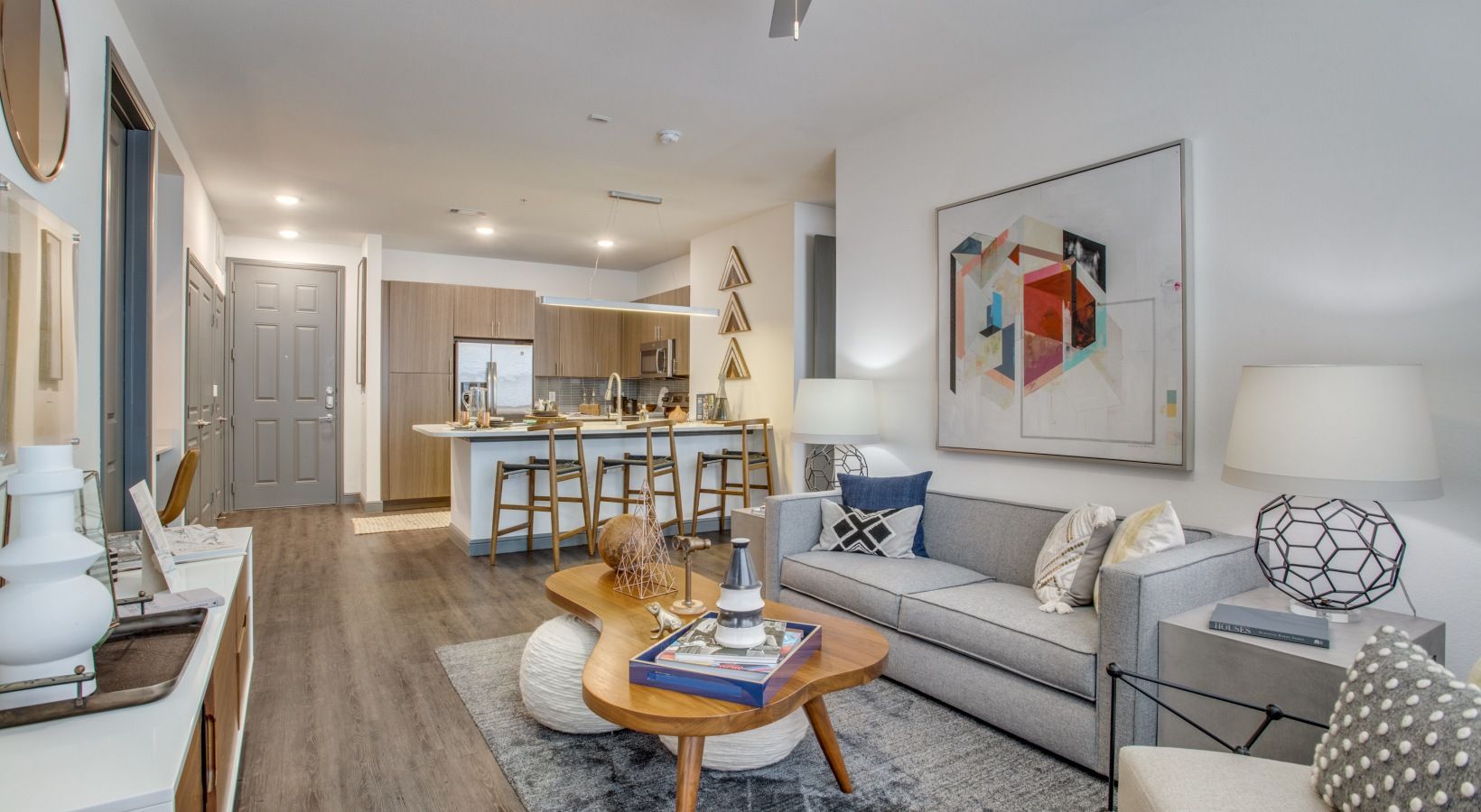 Bright modern living room with gray sofa, coffee table, wall art, and kitchen island in background