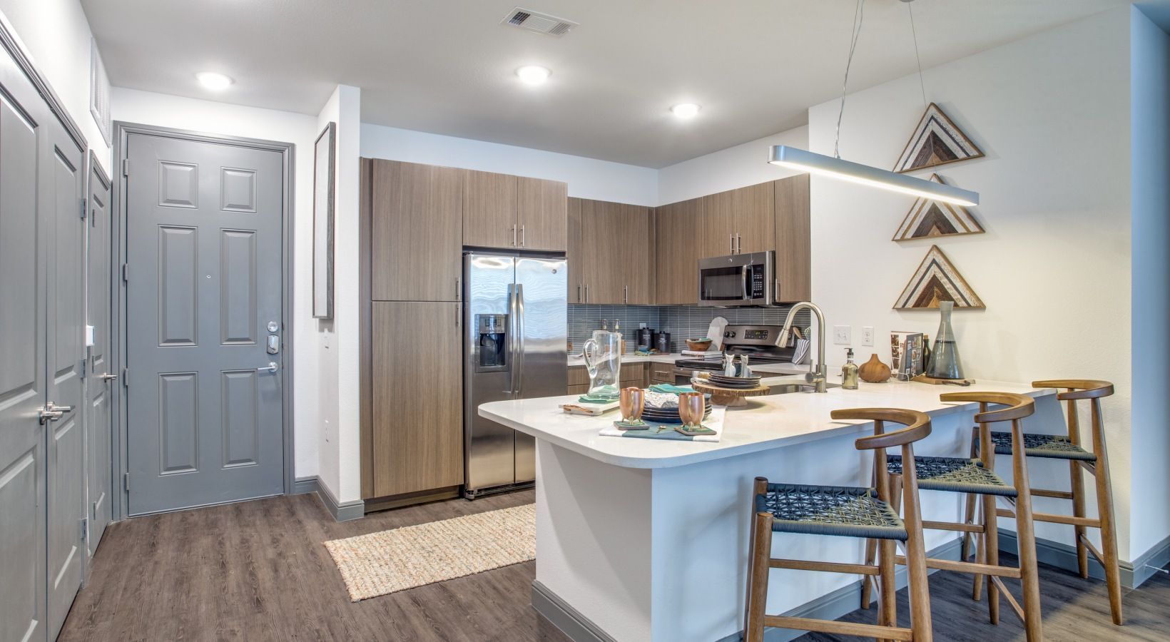 Modern kitchen with island, stainless fridge, bar stools, and triangular wall shelves in a bright open layout