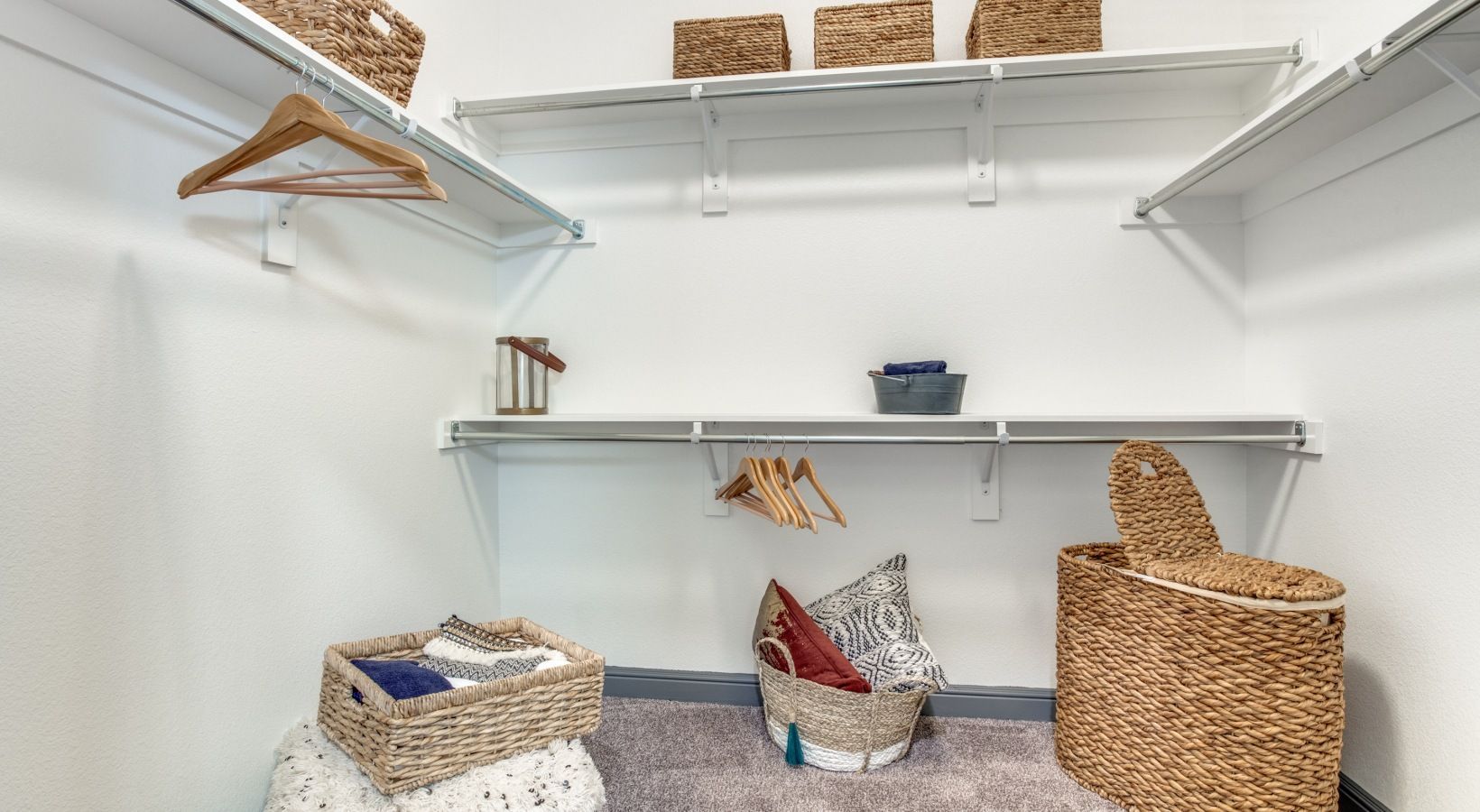 White closet shelves with baskets, folded clothes, and wicker storage bins on the floor