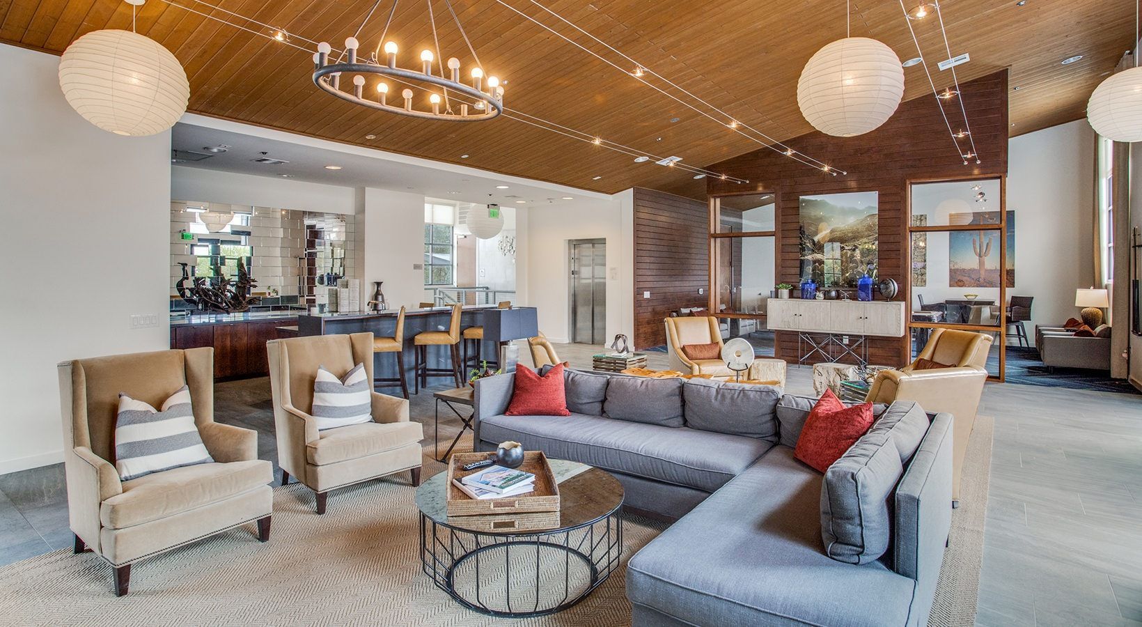 Spacious modern living room with gray sectional, armchairs, round tables, chandelier, and wood ceiling