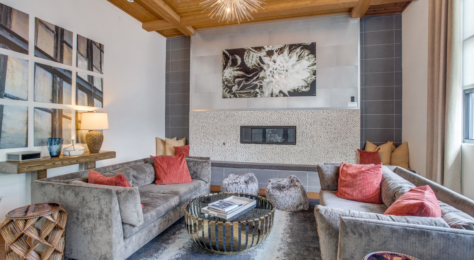 Modern living room with gray sofas, red accents, wooden ceiling, and a fireplace mantle