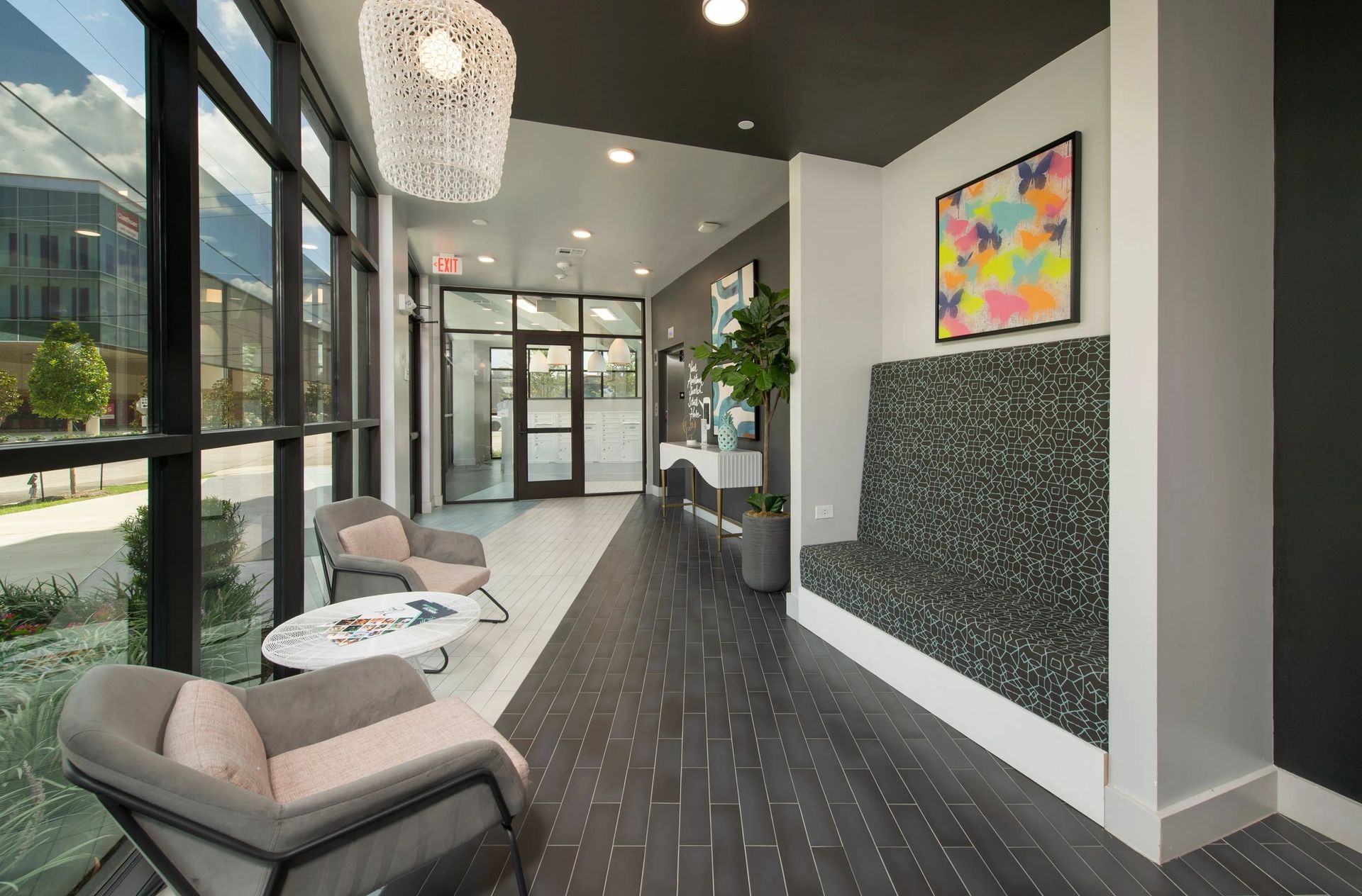 Modern apartment lobby with lounge chairs, large windows, pendant lights, and colorful wall art
