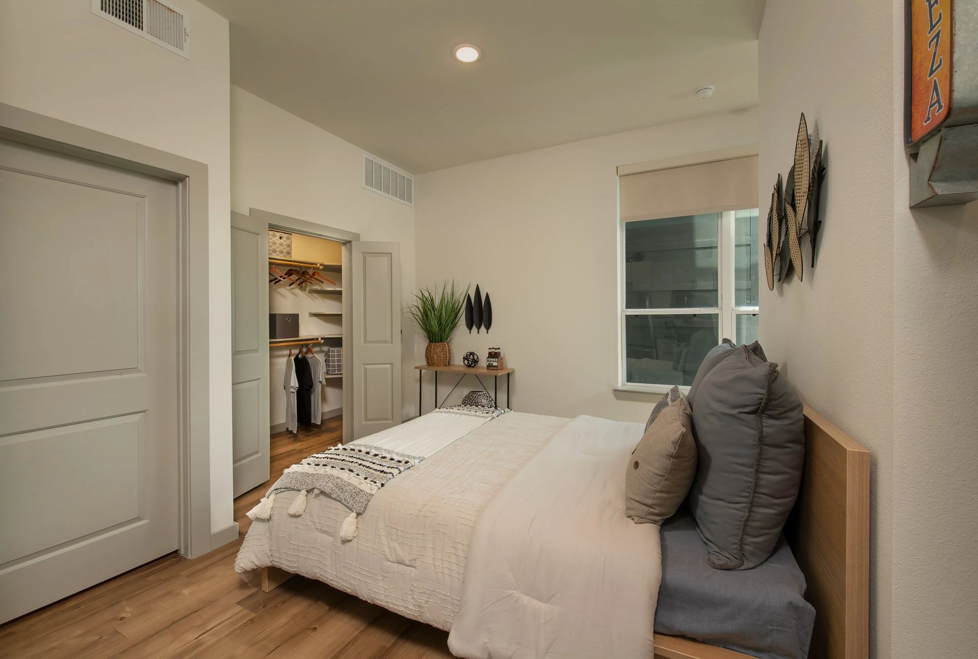 Modern bedroom with a neatly made bed, gray pillows, wood floors, and an open closet door
